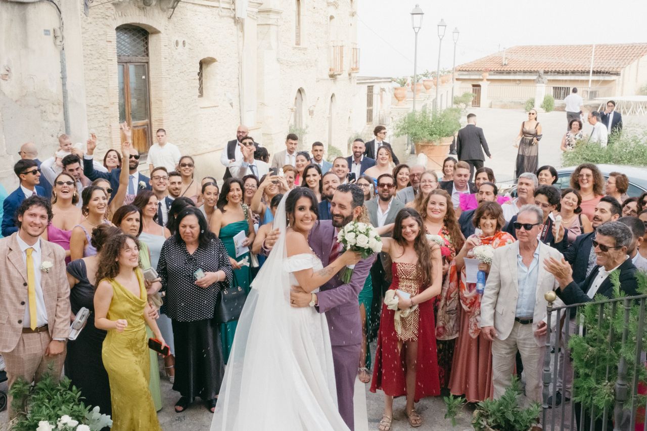 Wedding celebration with large crowd of guests in colorful attire outside historic venue.