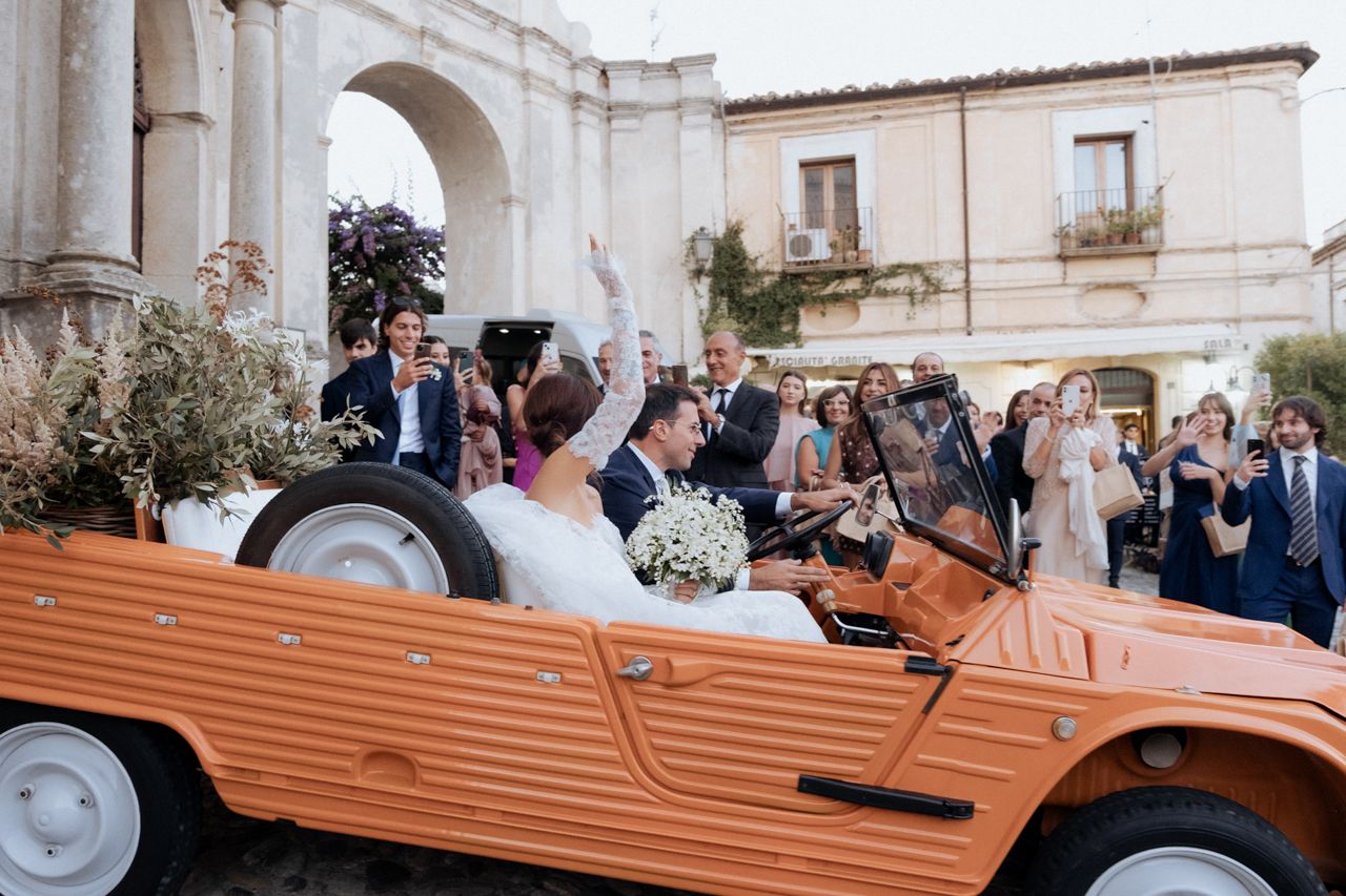 Couple rides in vintage orange convertible car after their wedding ceremony.