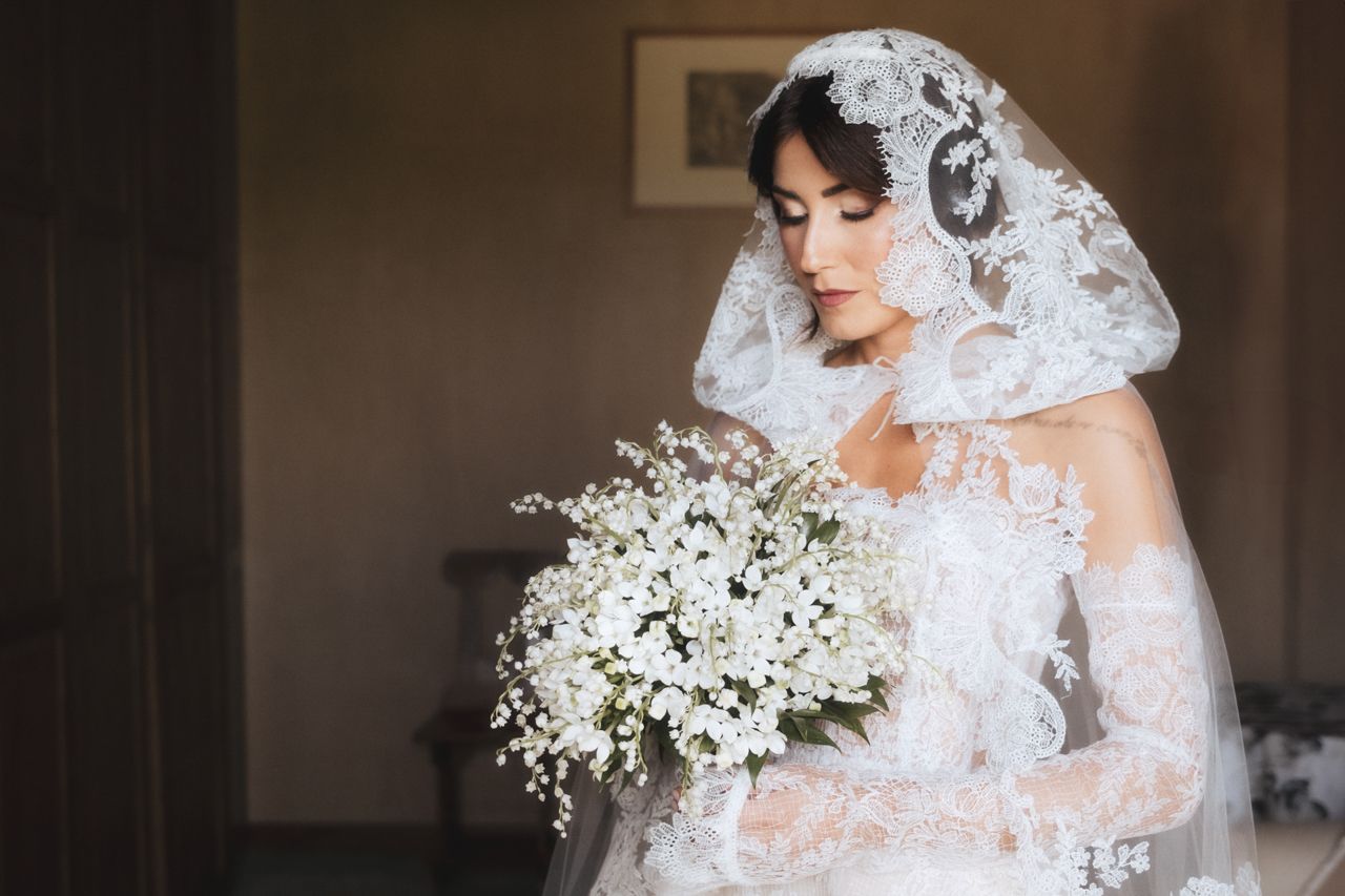 A romantic bridal portrait featuring a traditional lace veil and cascading white floral bouquet.
