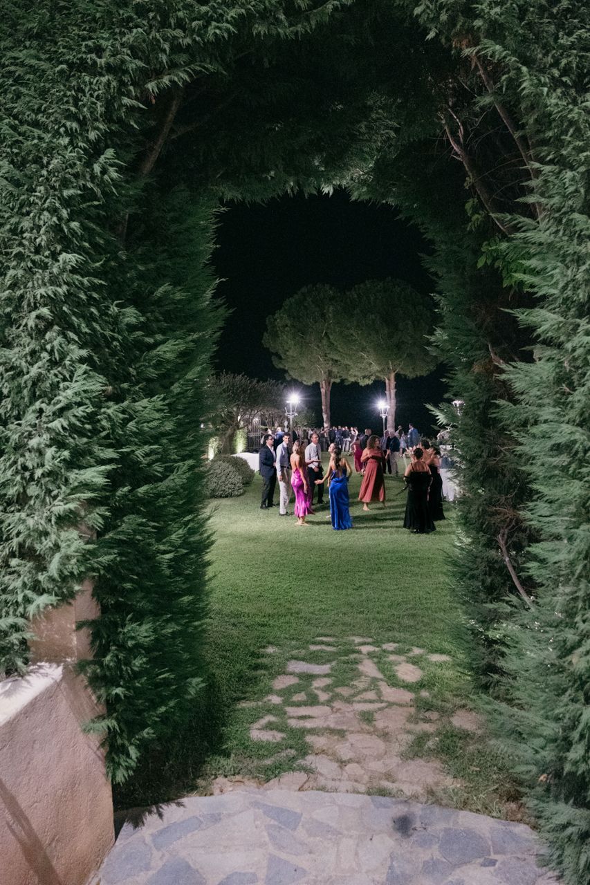 Wedding guests gather in an illuminated garden archway during an evening celebration.