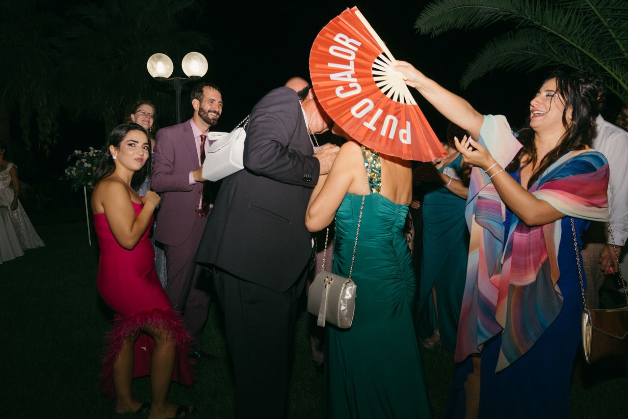 Party guests having fun with decorative fans at an outdoor evening celebration.