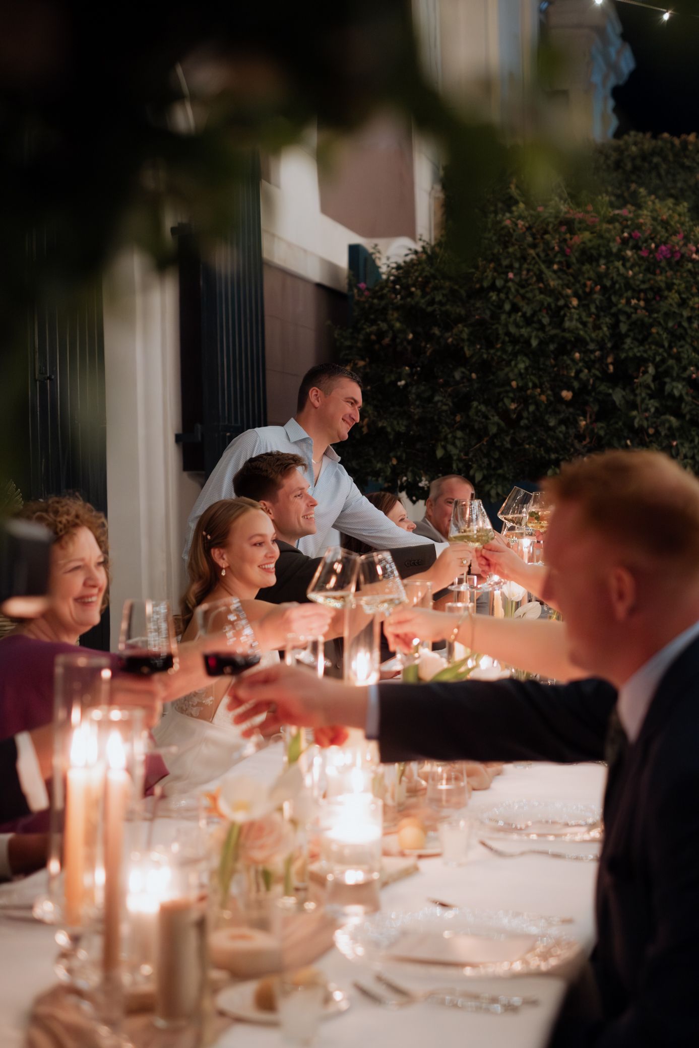 Elegant dinner party guests enjoying wine and conversation at a candlelit table with formal place settings.