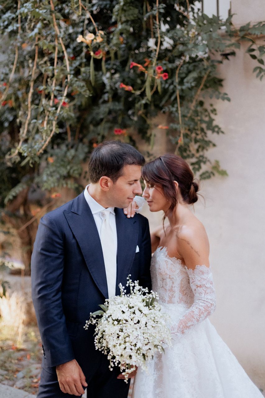 Newlyweds share intimate moment in garden setting with white floral bouquet.