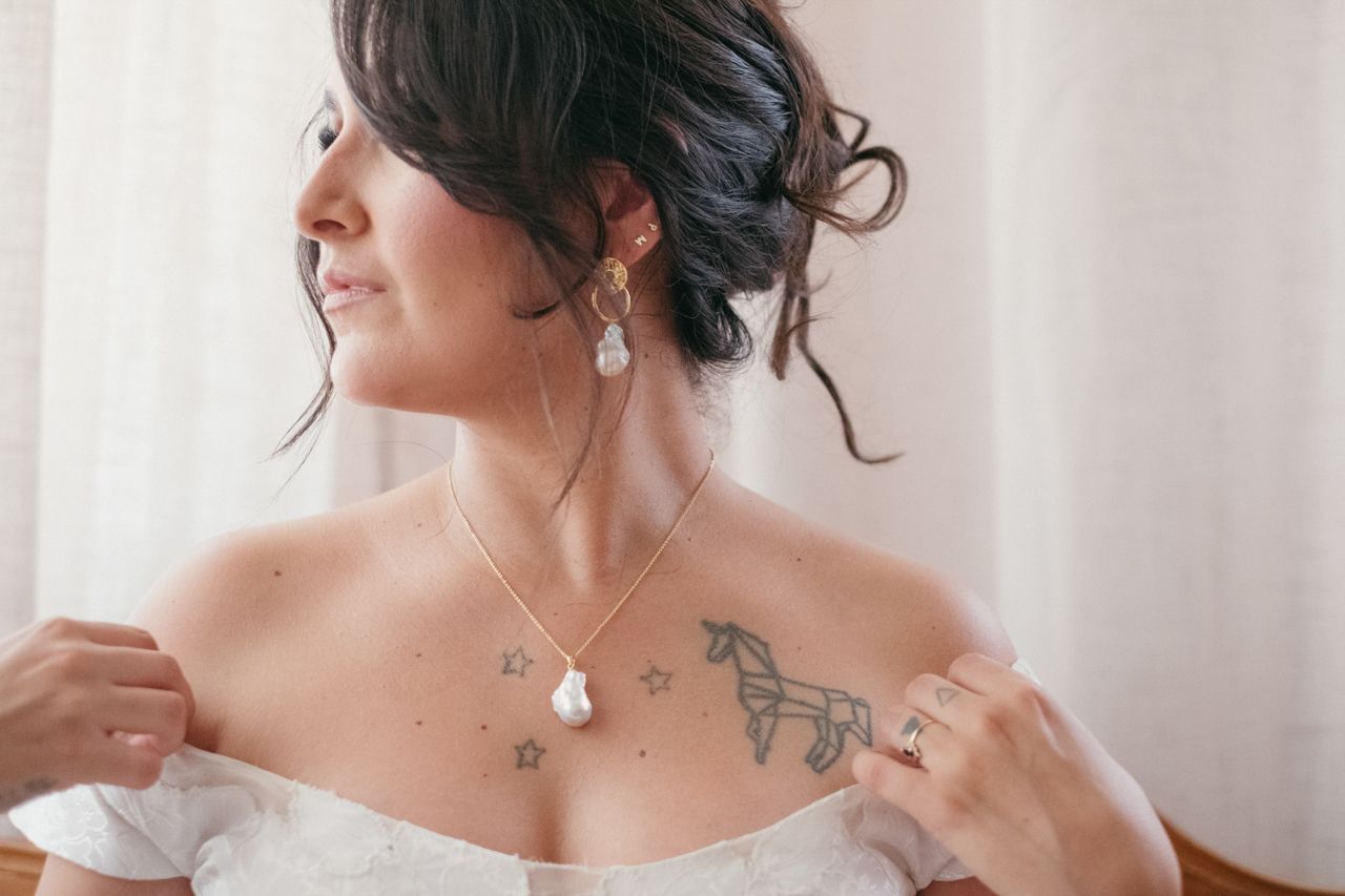 Bride wearing delicate jewelry and showing intricate tattoo detail on shoulder area.