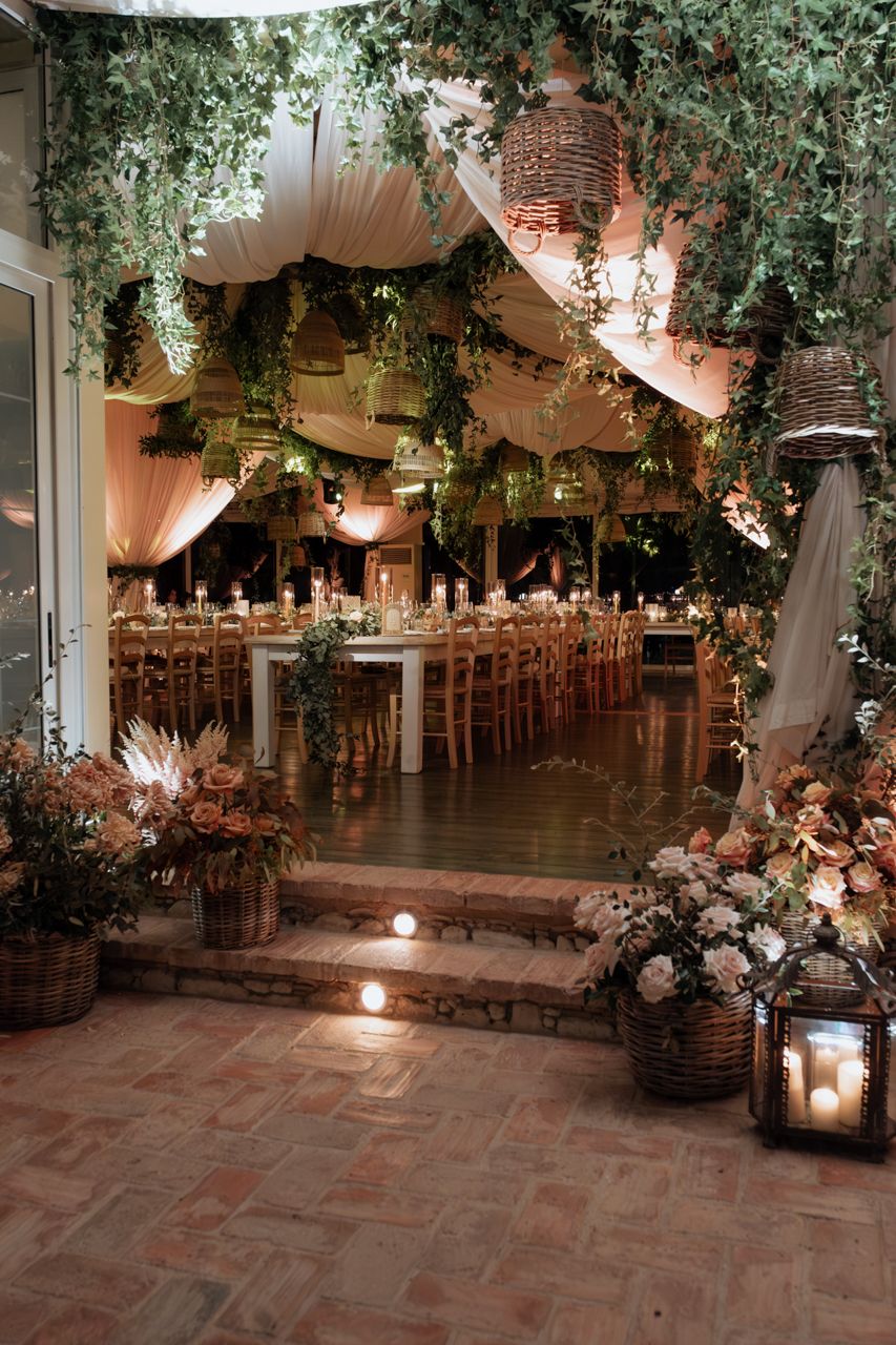Wedding reception space decorated with hanging lights, fabric draping and lush greenery.