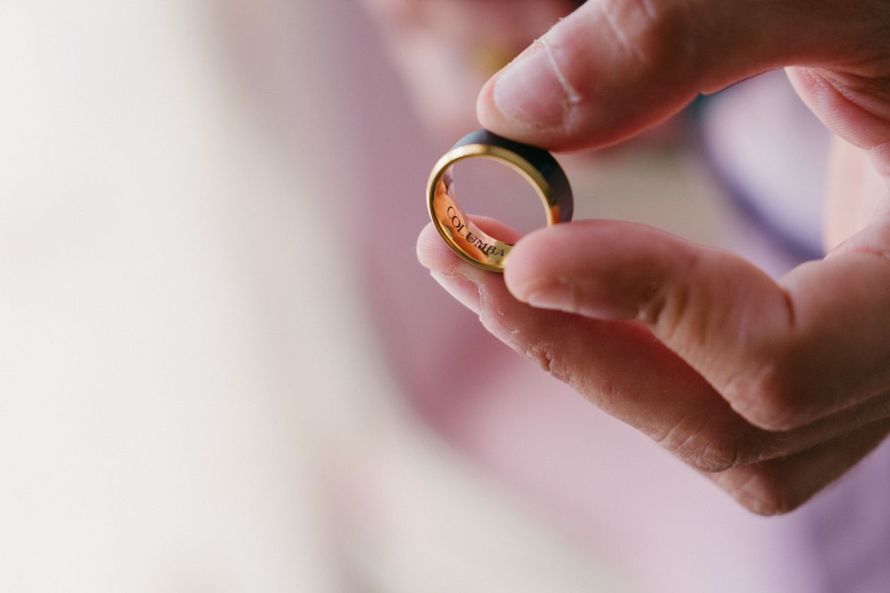 Close-up shot of hands holding a golden wedding ring against a soft blurred background.