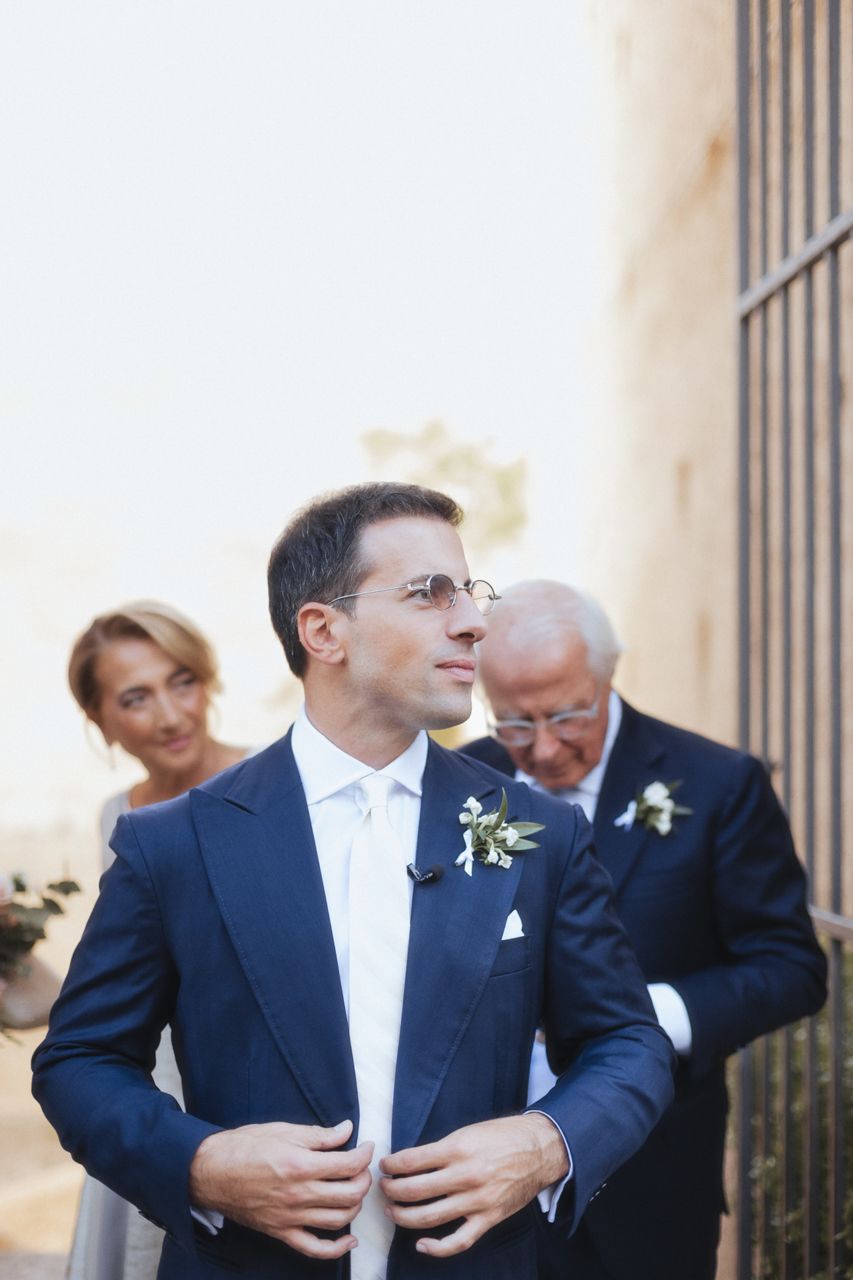 Wedding party members in formal attire gather outside a stone building.