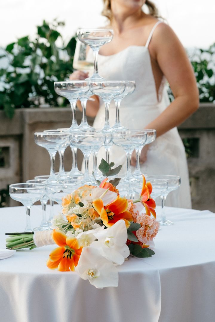 Champagne tower with orange and white floral decorations on an elegant white tablecloth.