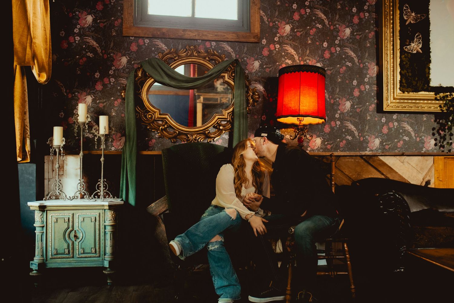 Restaurant interior featuring red lamp shades and floral wallpaper in moody lighting.
