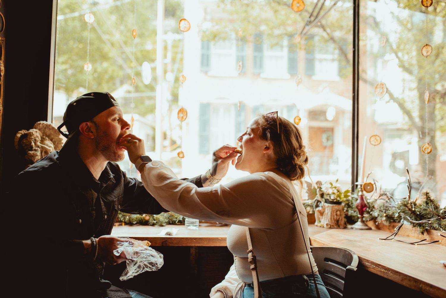 Couple playfully feeding each other at a sunlit restaurant table.