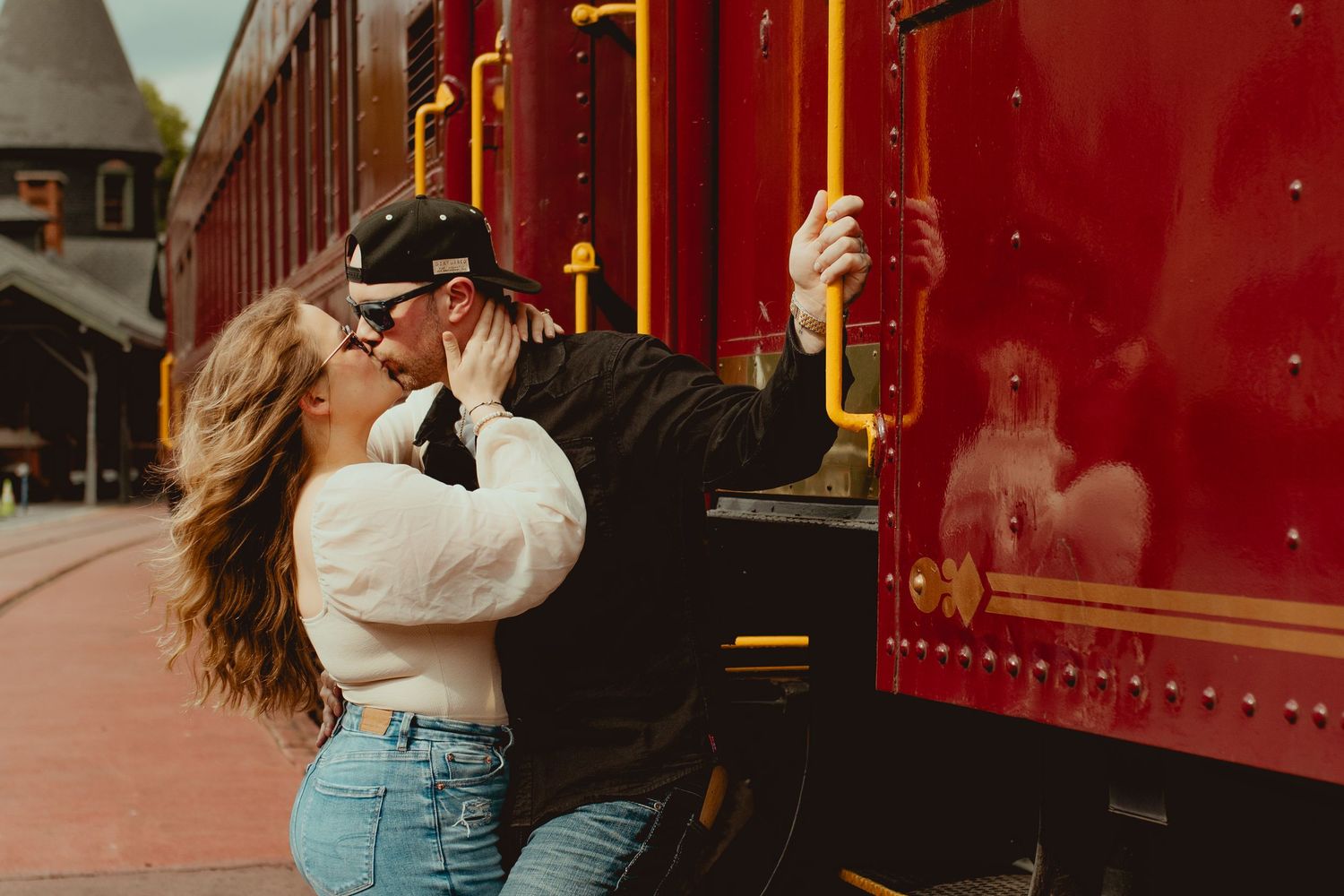 Romantic embrace alongside a vintage red train car on a sunny day.