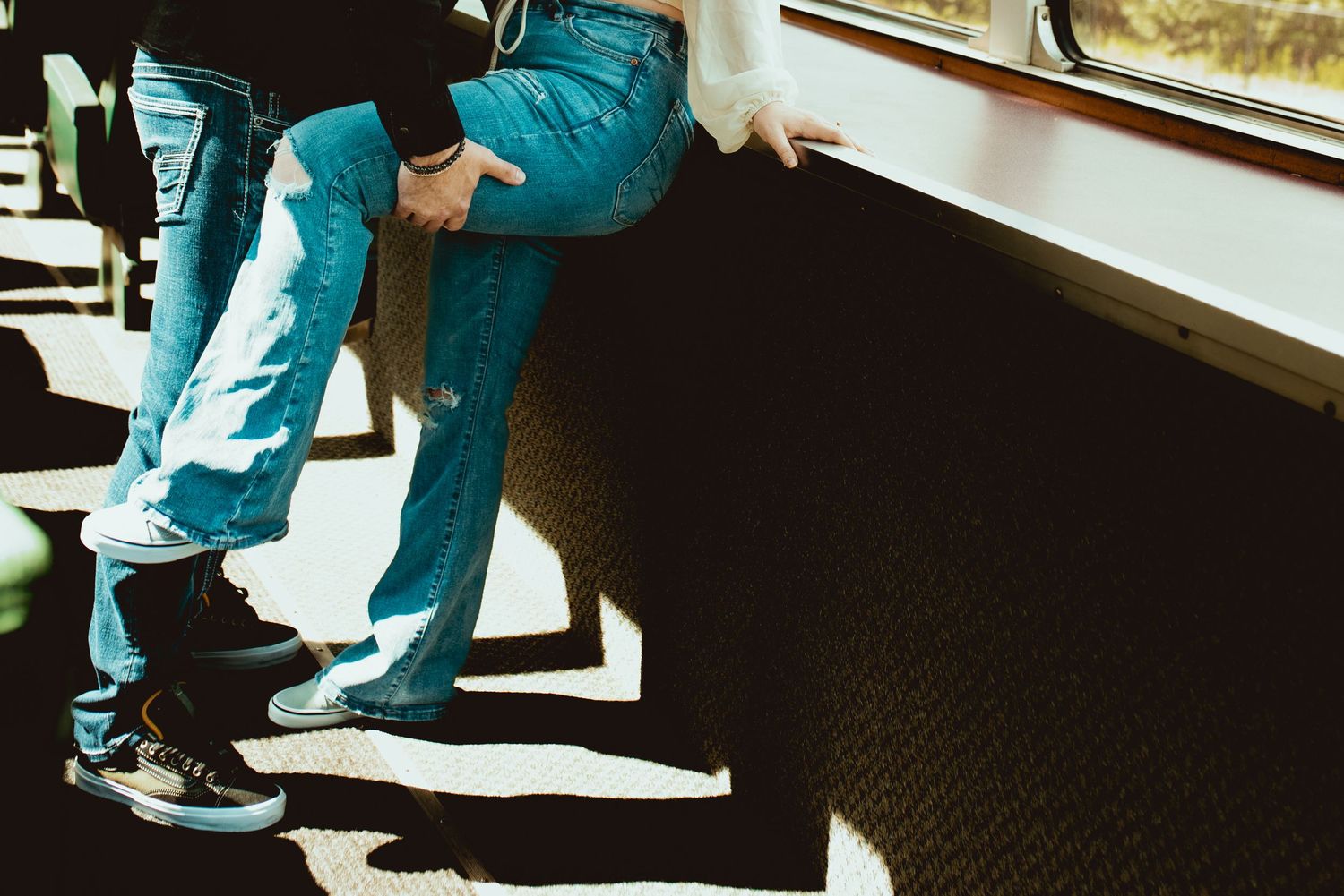 Cropped view of couple's legs standing in a sunlit train car interior.