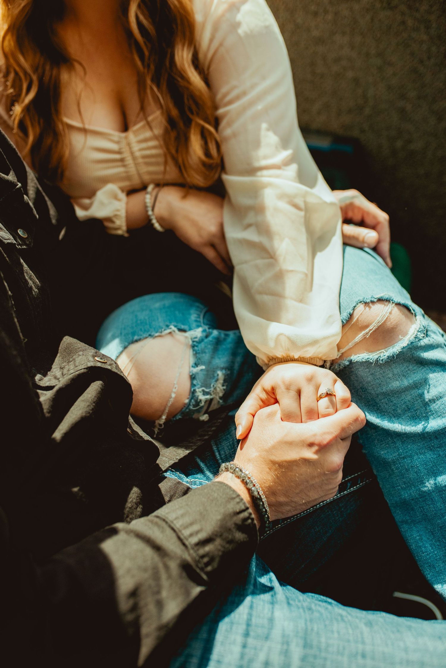 Couple holding hands while sitting in ripped jeans on train.