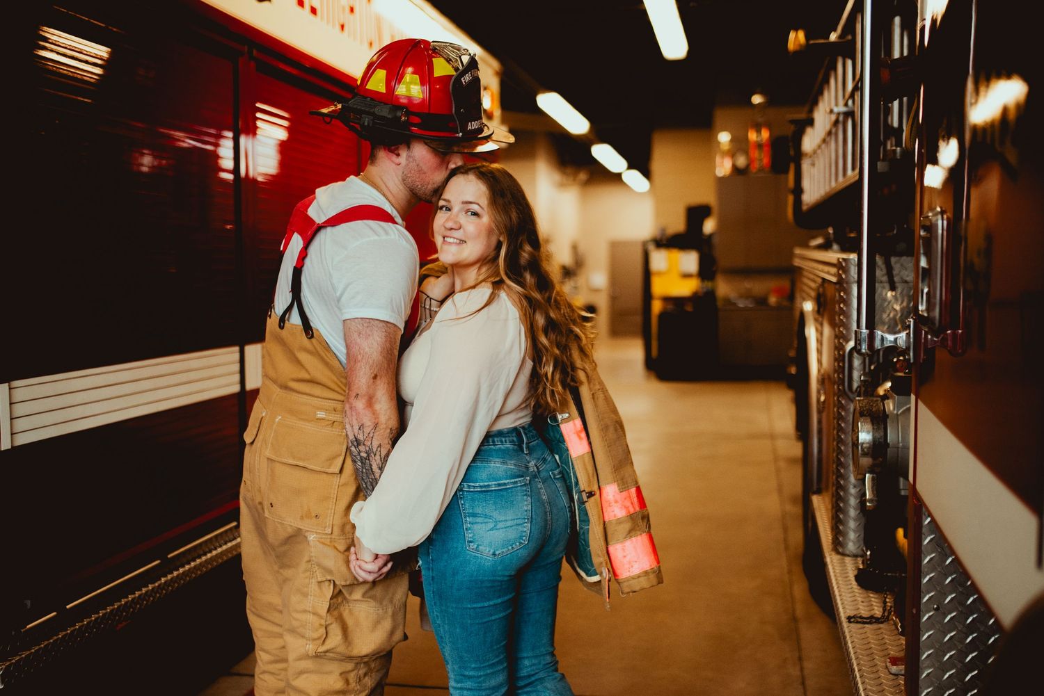 A couple in firefighting attire shares an intimate moment beside their fire engine.