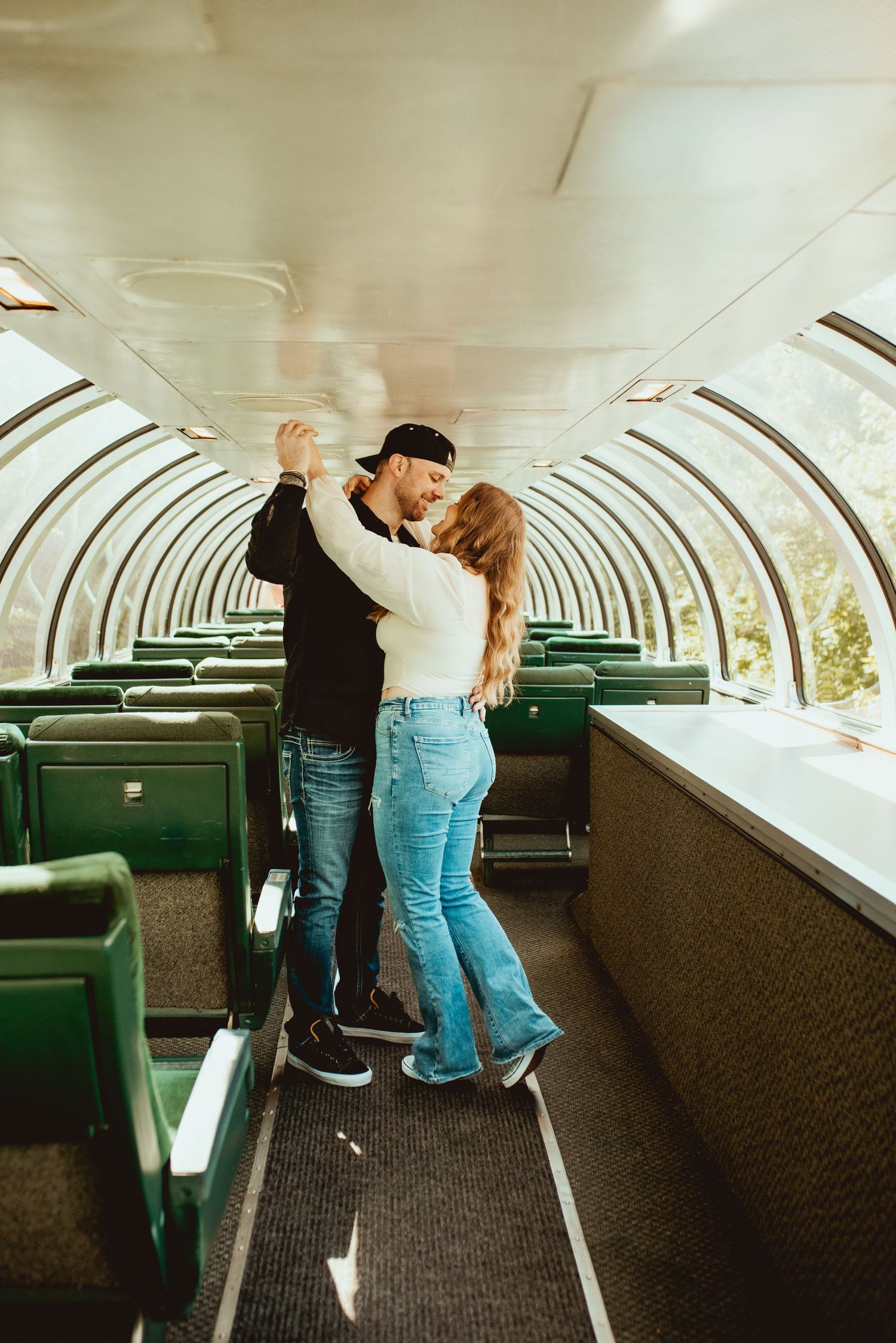 A romantic dance pose in a sunlit vintage train observation car with green seats.