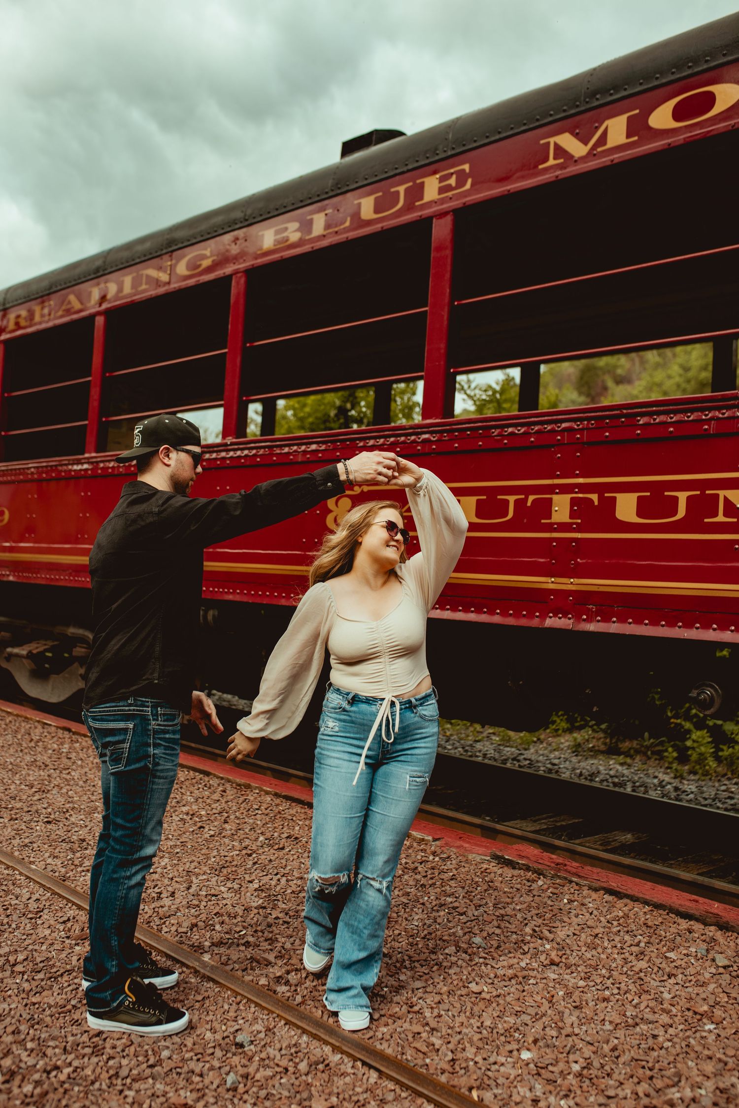 A couple poses in front of a classic red train car called Blue Mountain Railroad.