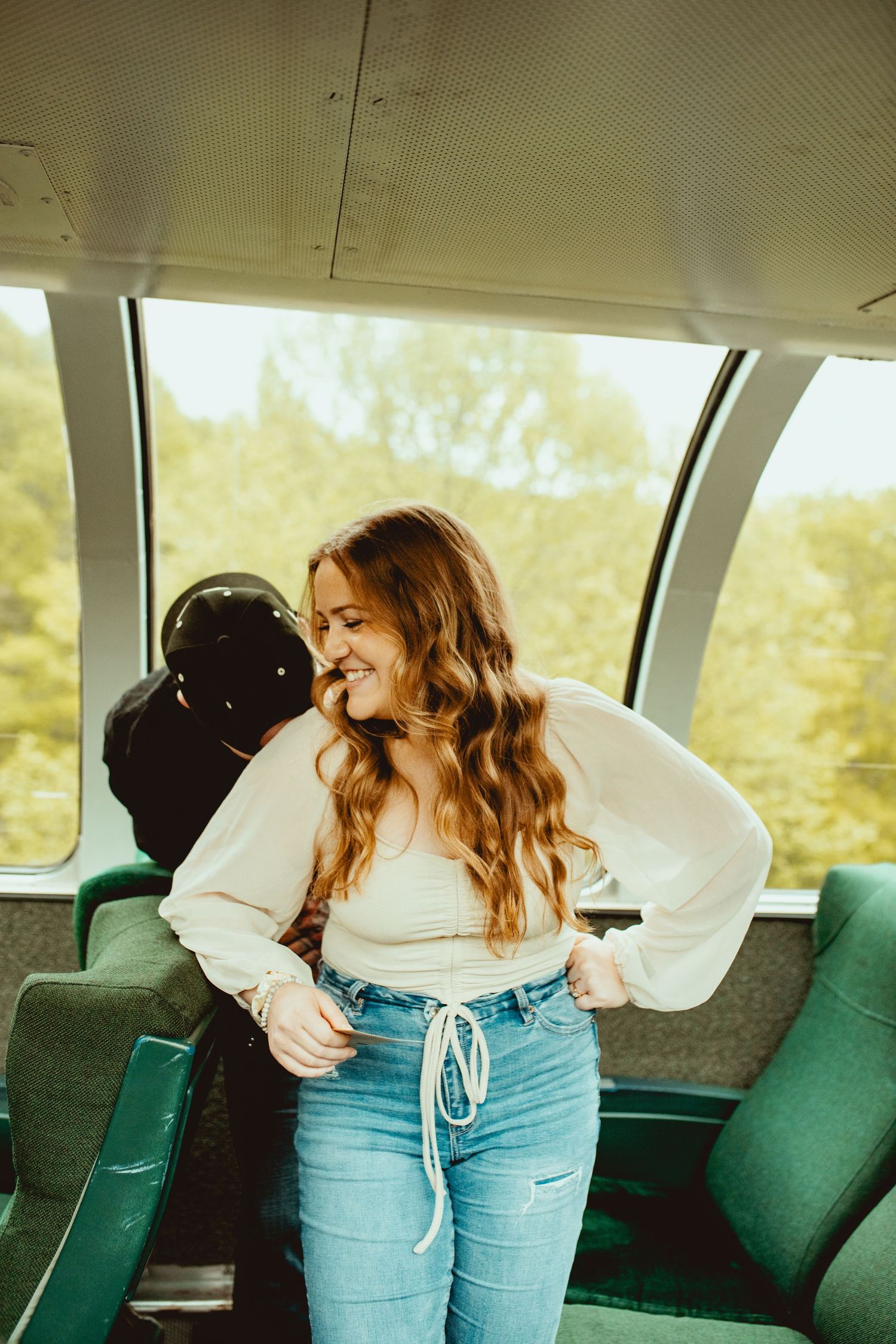 Woman in white shirt and jeans sitting in a vintage train car with emerald seats.