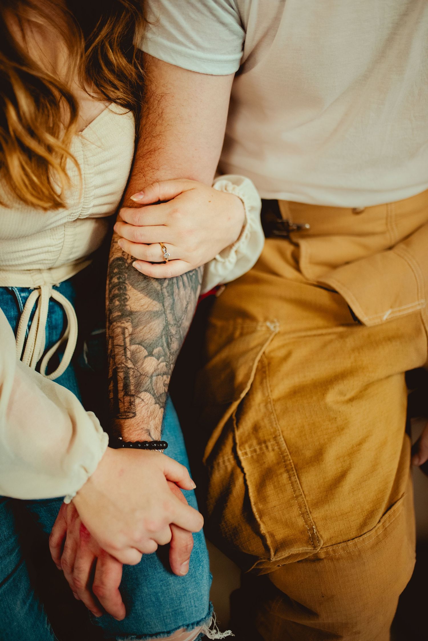 Close-up of tattooed arms and hands showing engagement ring at fire station.