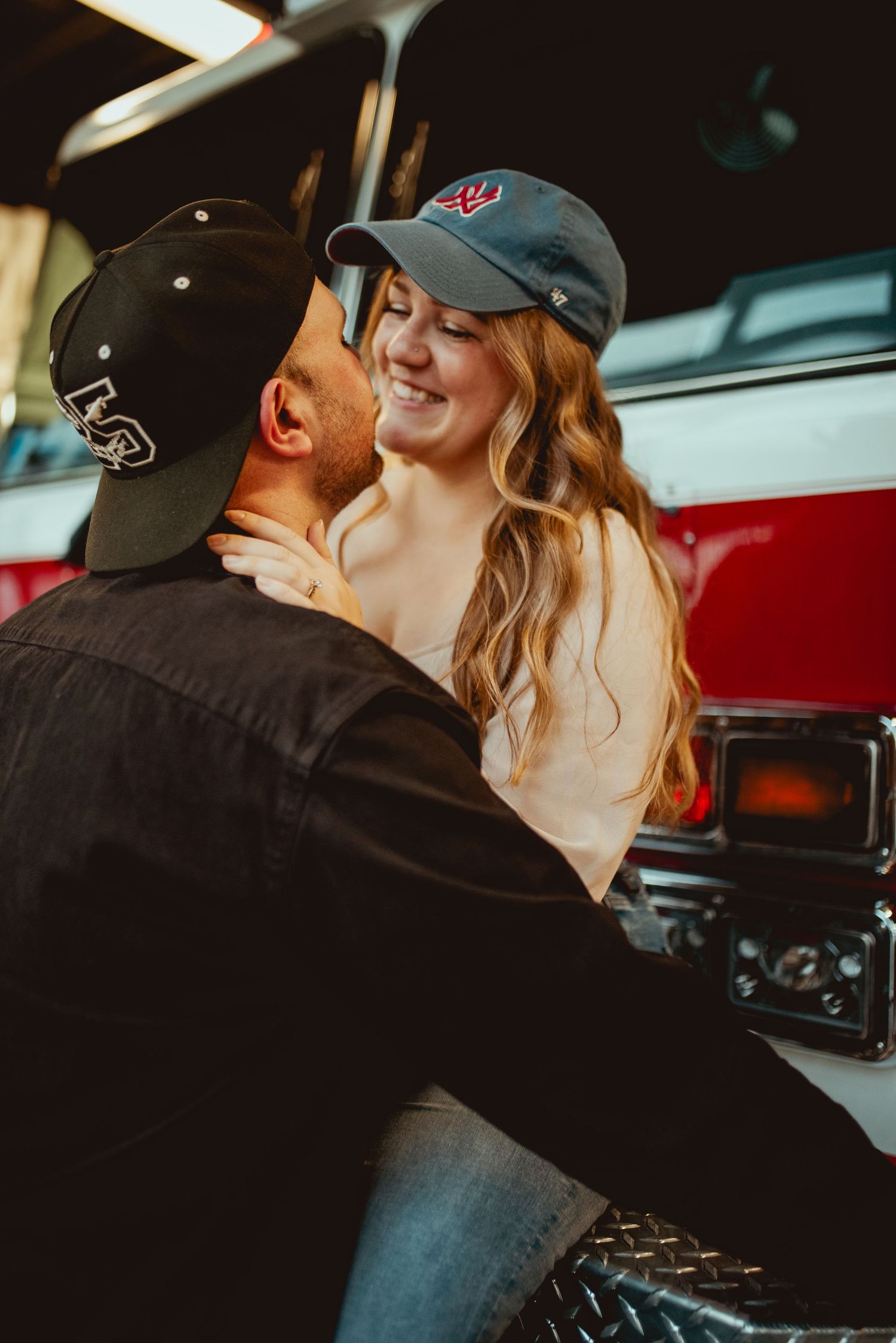Couple sharing playful moment in front of red fire engine.
