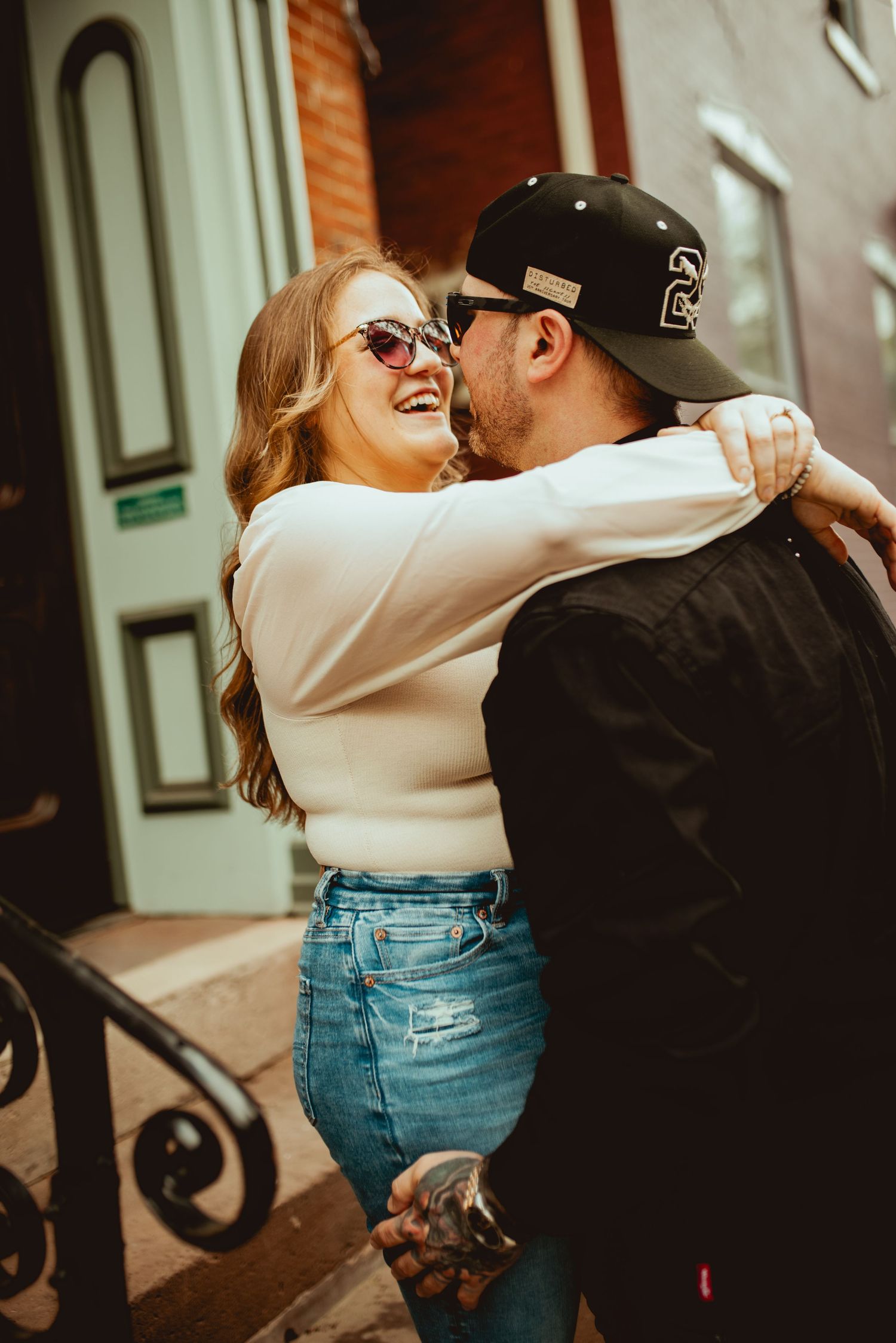 Joyful couple embracing on urban steps with classic architecture in background.