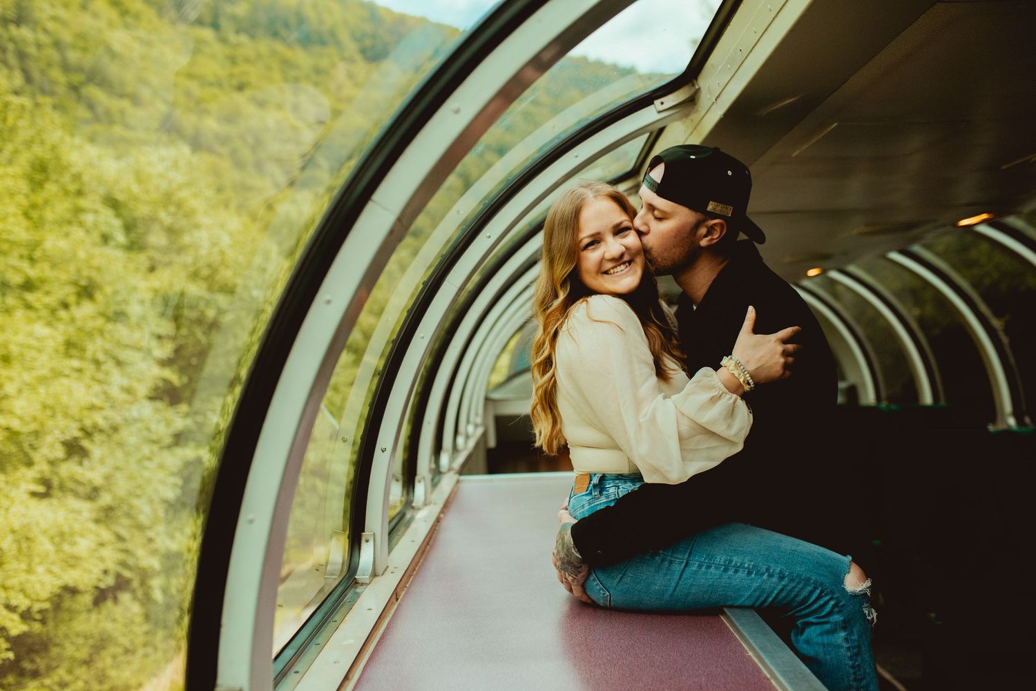 Romantic couple embracing in panoramic train car with mountain views.