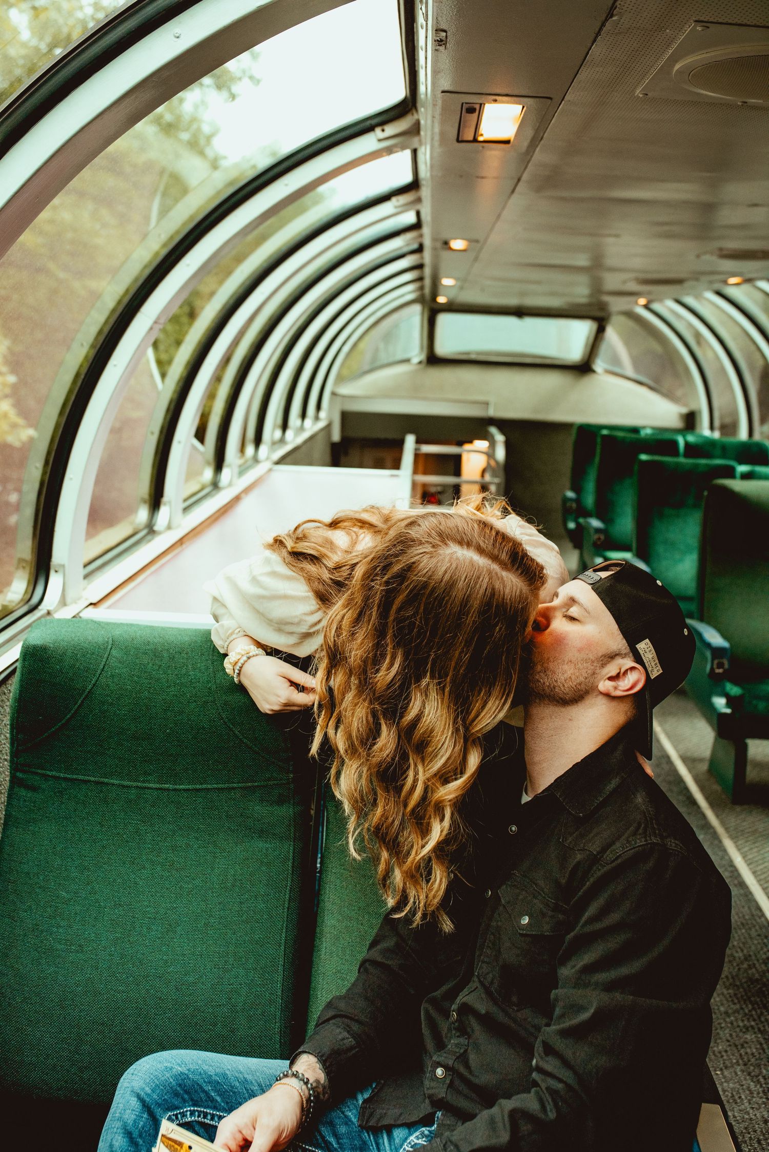 Tender moment shared between passengers in a vintage observation car with panoramic windows.