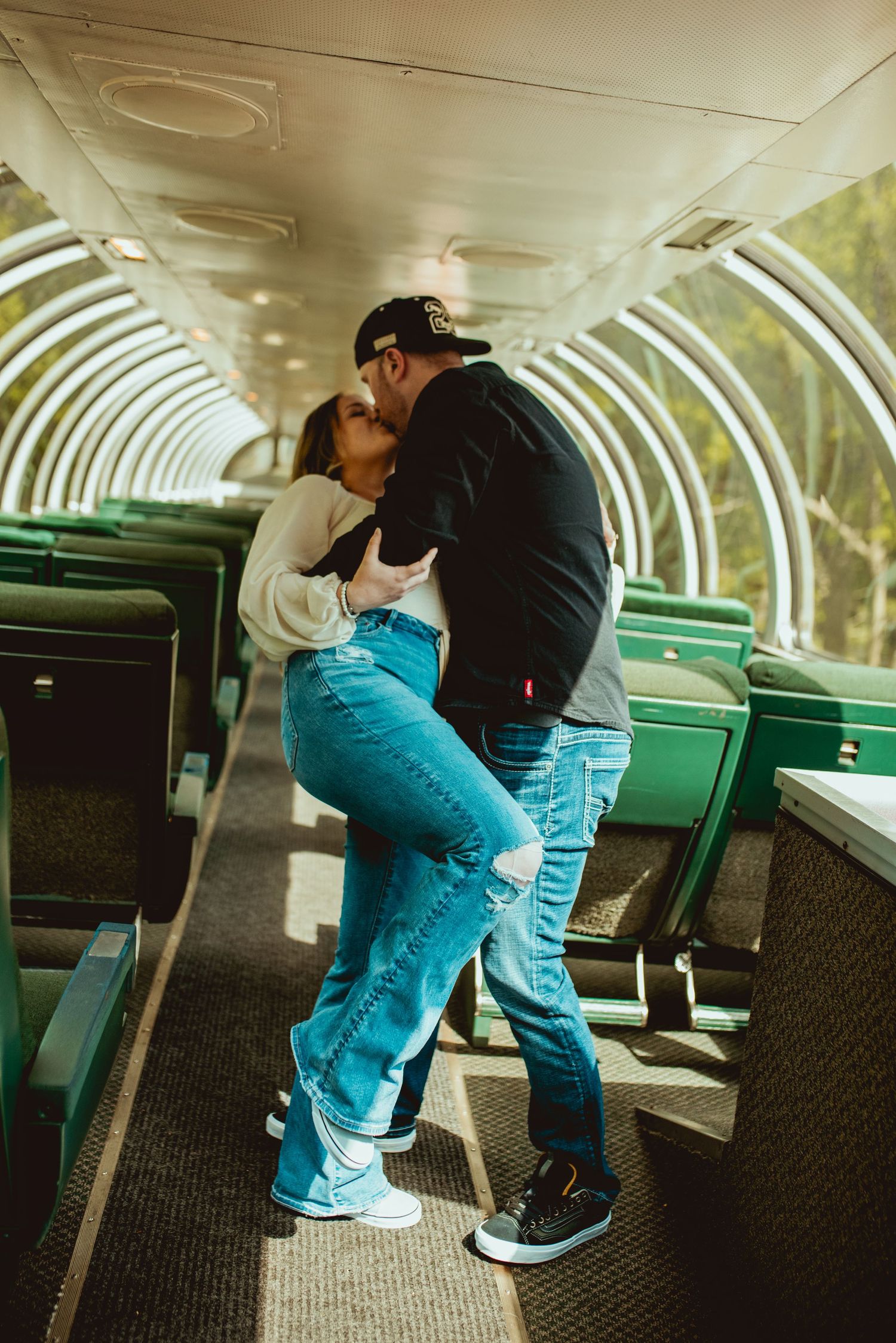 Romantic embrace in sunlit train car with green vintage seats.