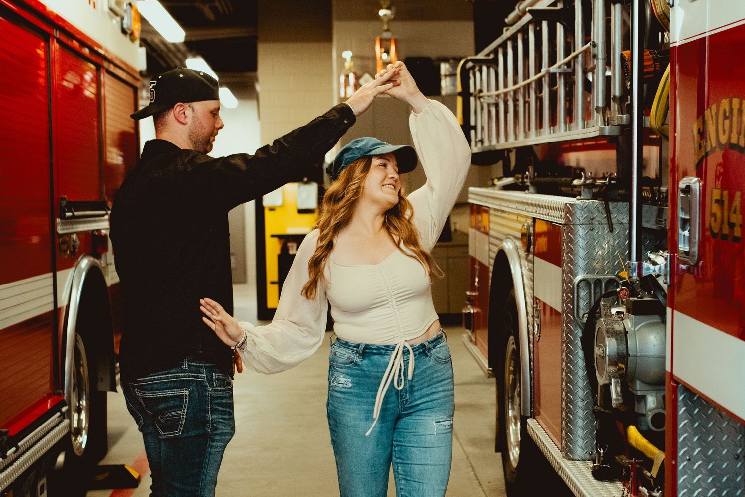 Dancing couple in casual wear at fire station between trucks.