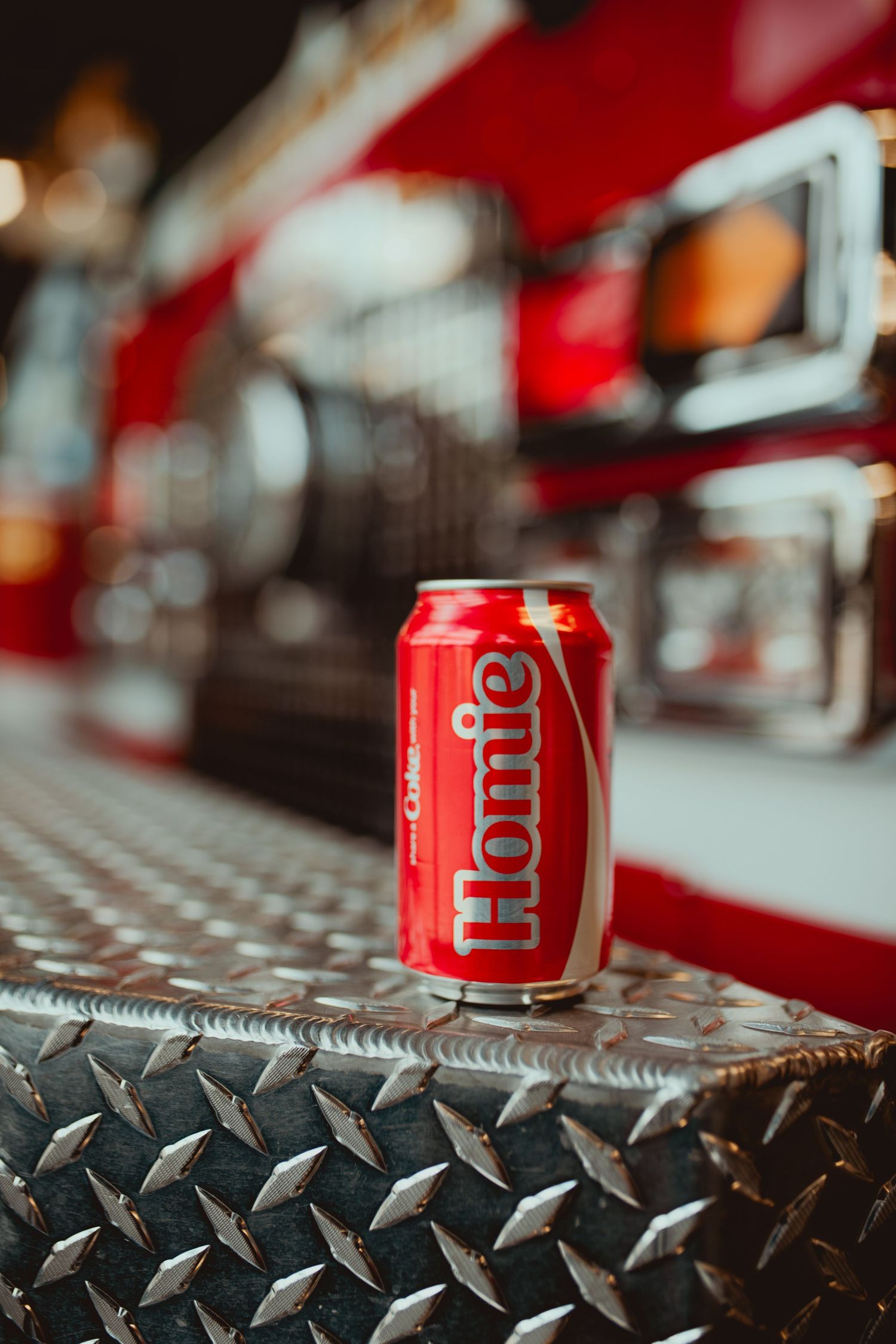 Close-up shot of a red Coca Cola can on a textured metal surface with shallow depth of field.