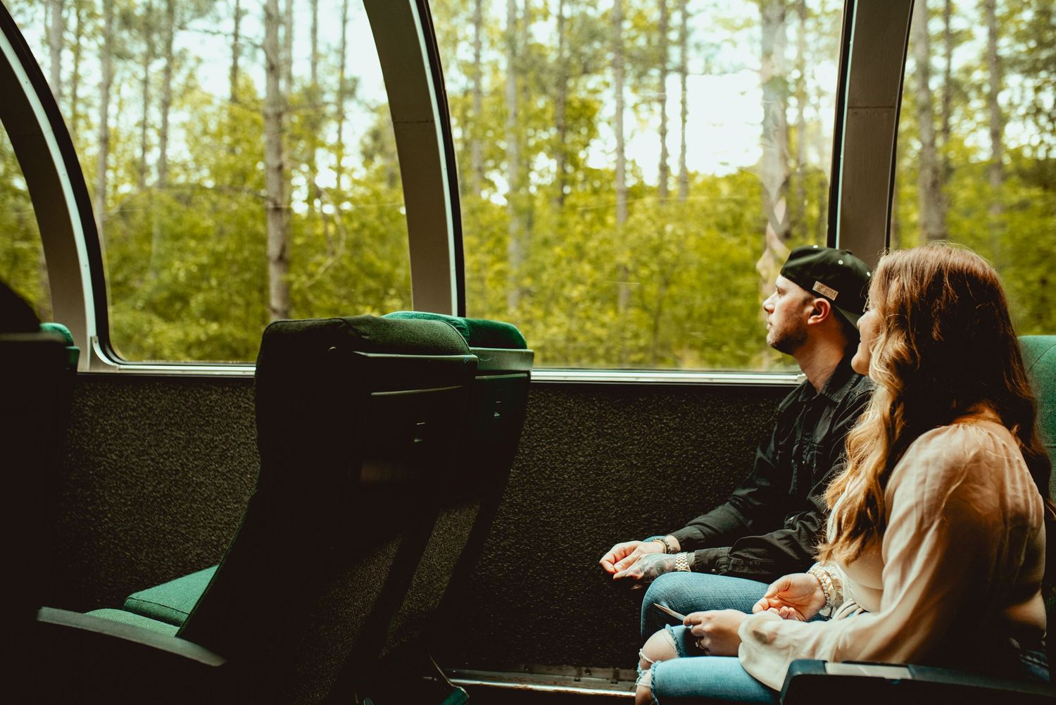 Passengers embrace on a scenic train journey through a forested landscape.