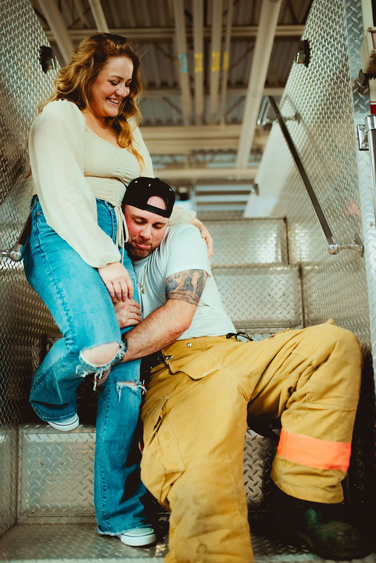 A couple embraces while sitting on the metal stairs of a fire truck.