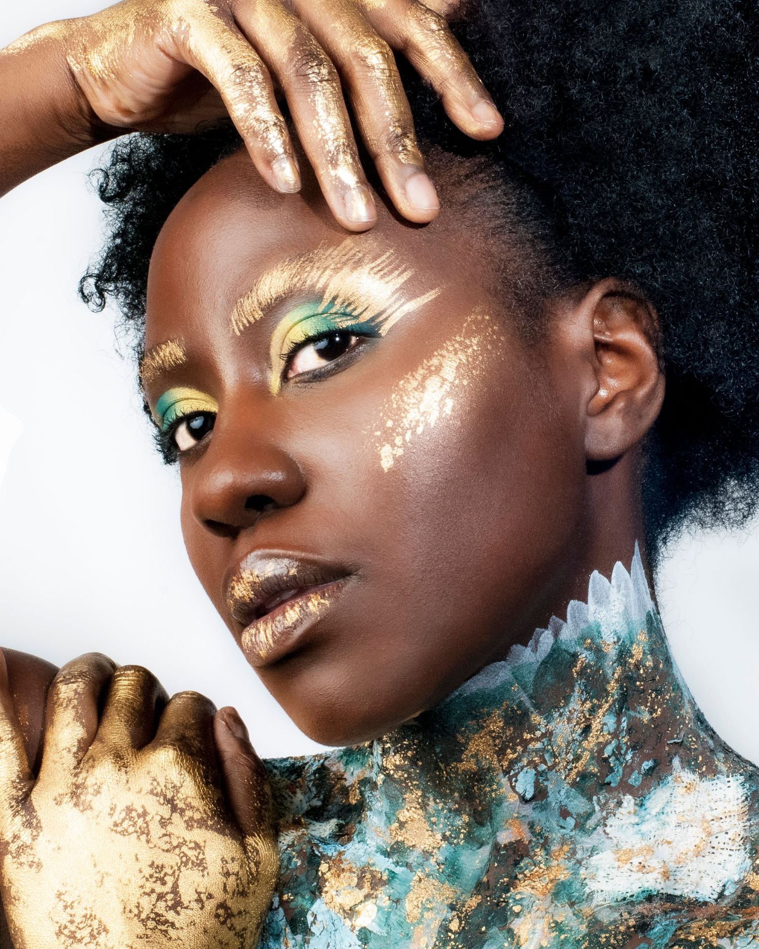 Artistic beauty photo with gold-painted hands and vibrant eye makeup.