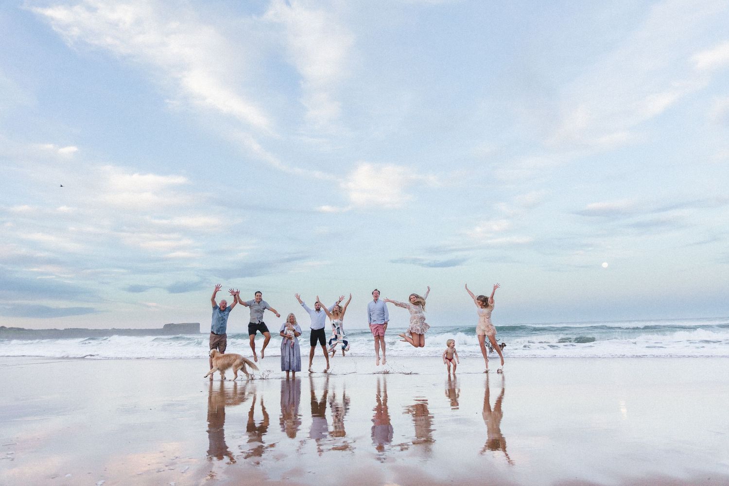 Group silhouettes jumping on beach at sunset with reflections in Kiama