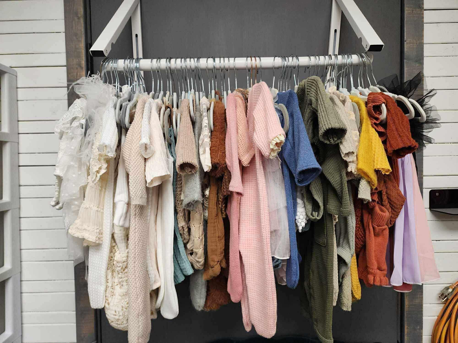 Clothing rack displaying various pastel and neutral colored garments hanging outdoors.