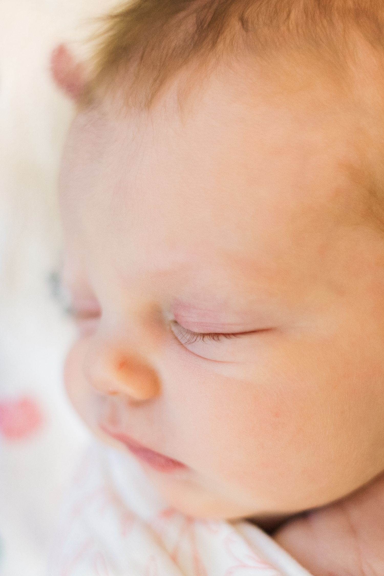 Ethereal close-up of sleeping baby with soft peachy skin tones.