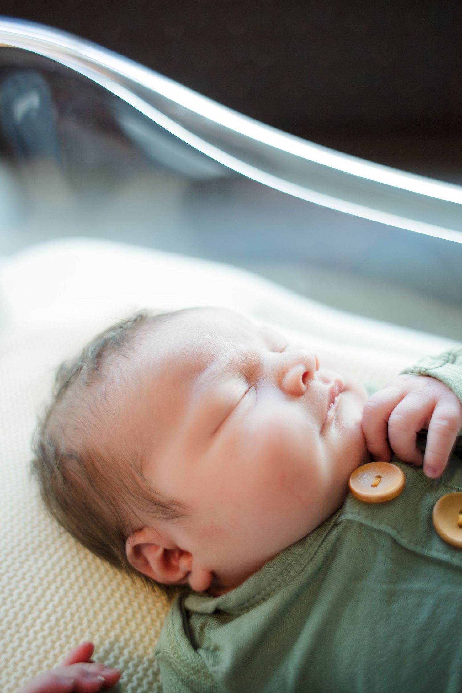 A sleeping baby in green clothing lies peacefully on a textured beige surface.