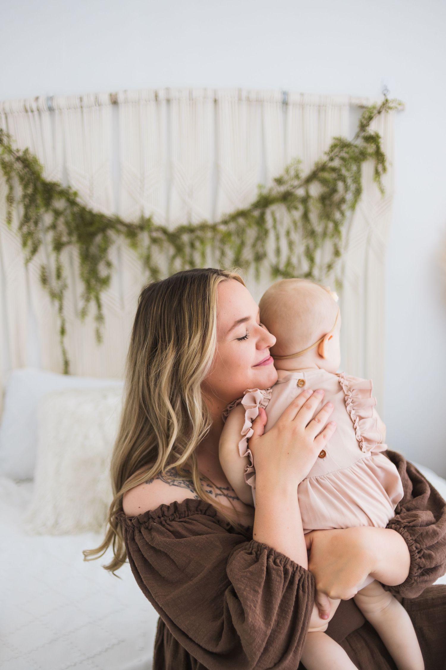 Sweet embrace between parent and infant against white backdrop with hanging greenery garland.
