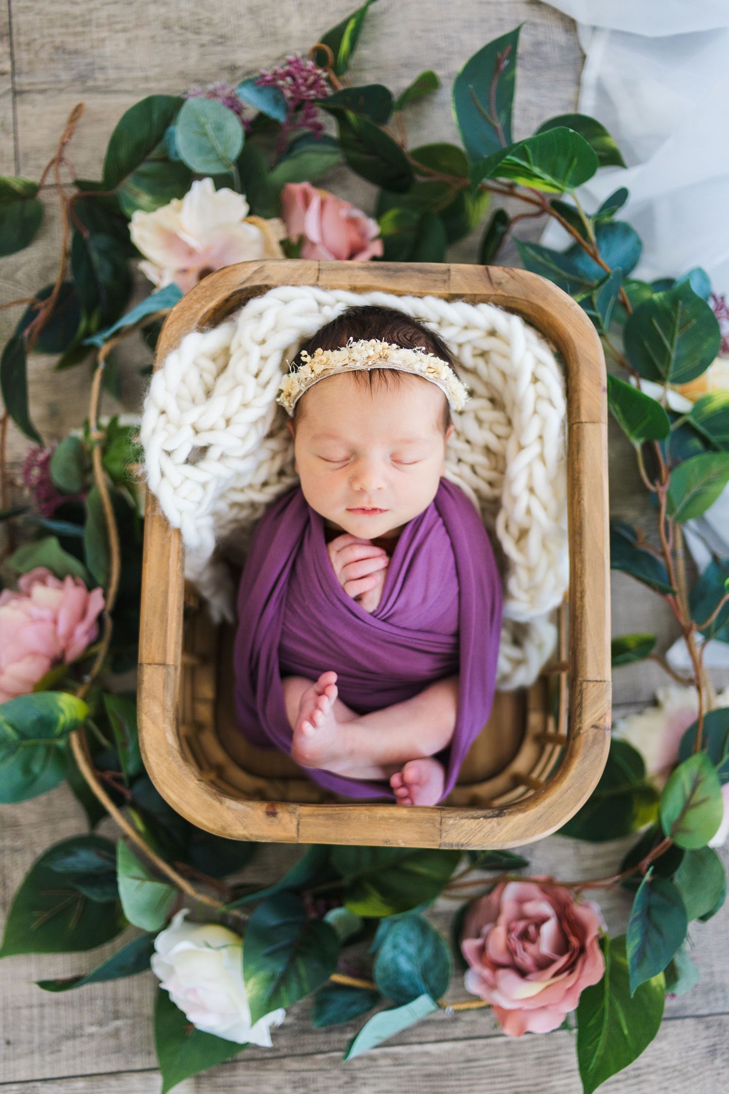 Newborn girl wrapped in purple swaddle surrounded by florals – Springfield MO studio photographer