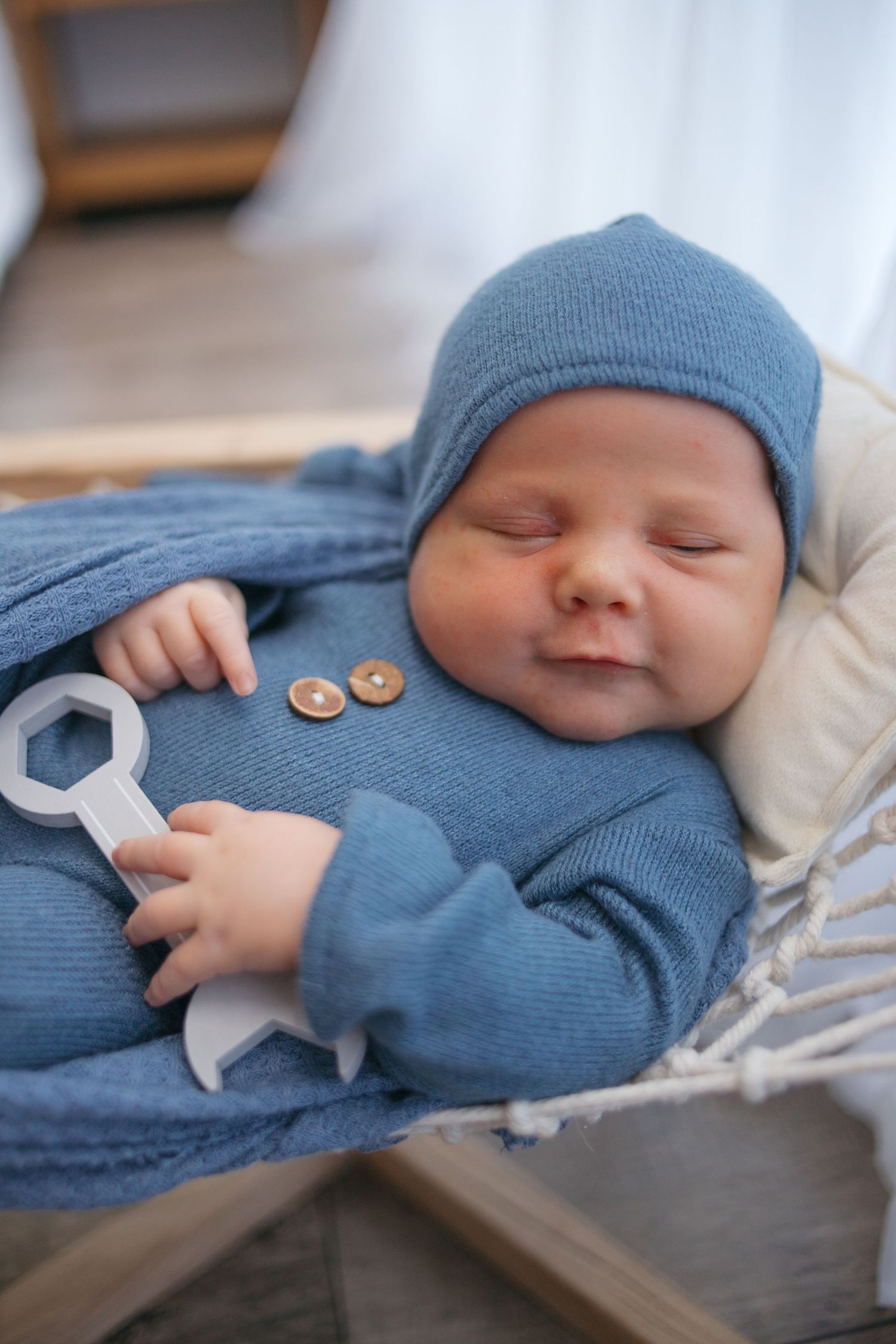 Close up of peaceful sleeping newborn wearing blue hat and outfit on wooden prop bed.