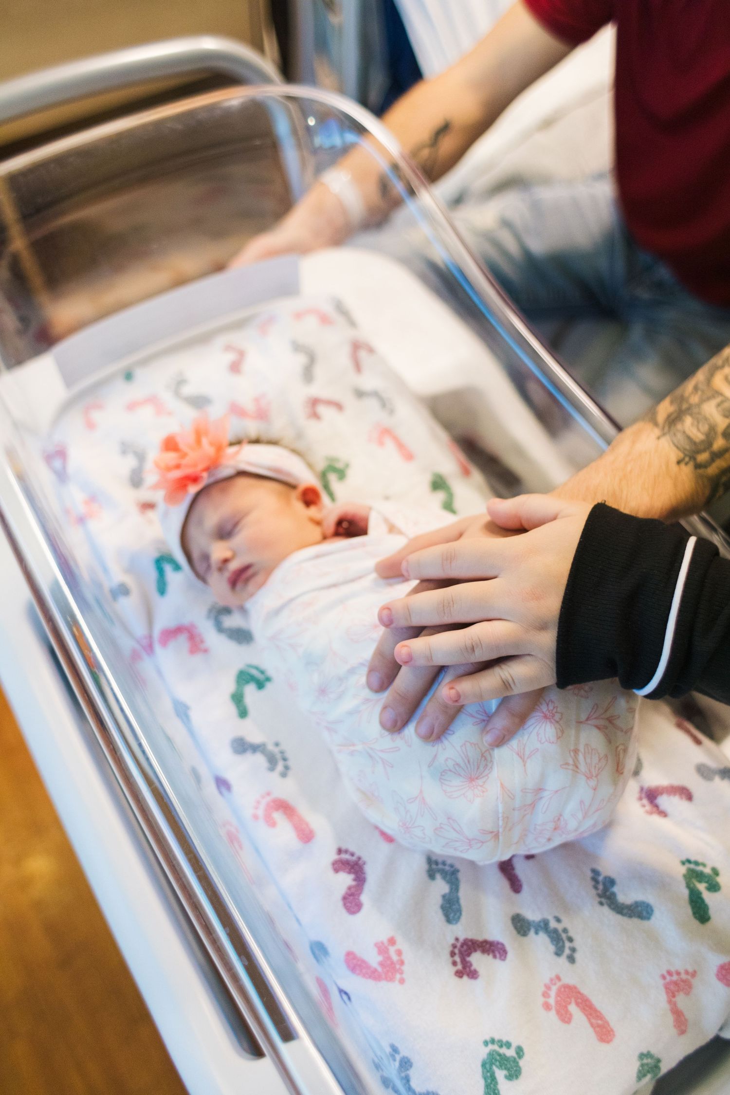 Newborn baby in hospital bassinet with colorful footprint patterned blanket.