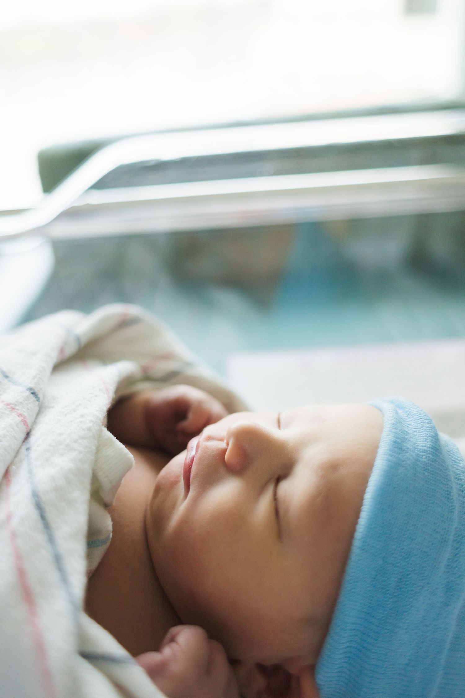 Peaceful sleeping newborn with blue cap in hospital bassinet.