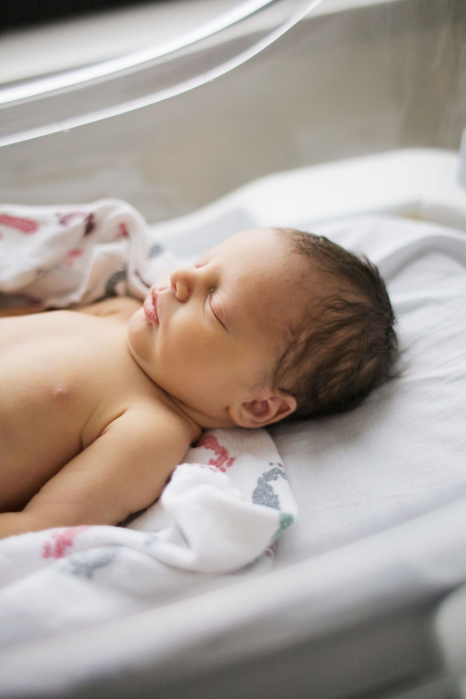 Sleeping newborn baby resting peacefully on white hospital linens.