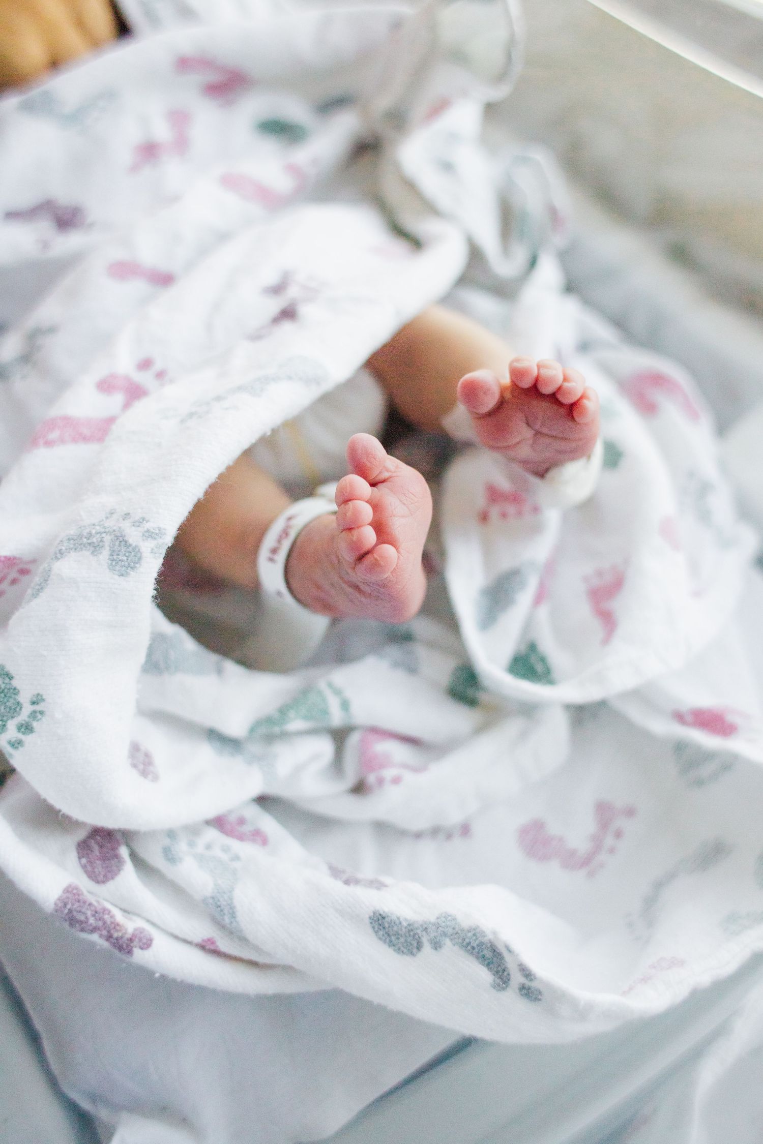 Close-up of tiny newborn baby feet on floral patterned white blanket.