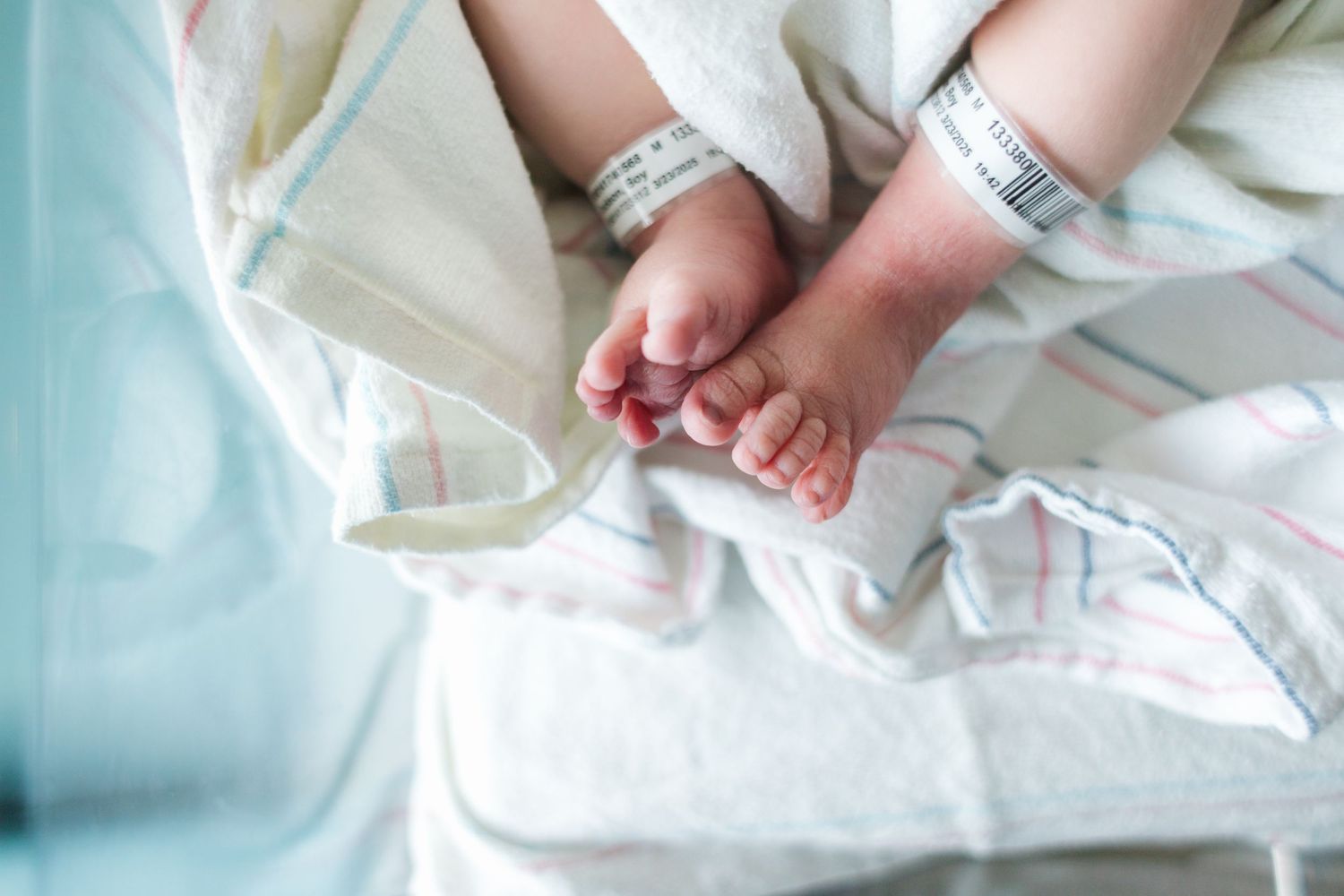 Hospital identification bracelets on tiny newborn feet wrapped in white blanket.