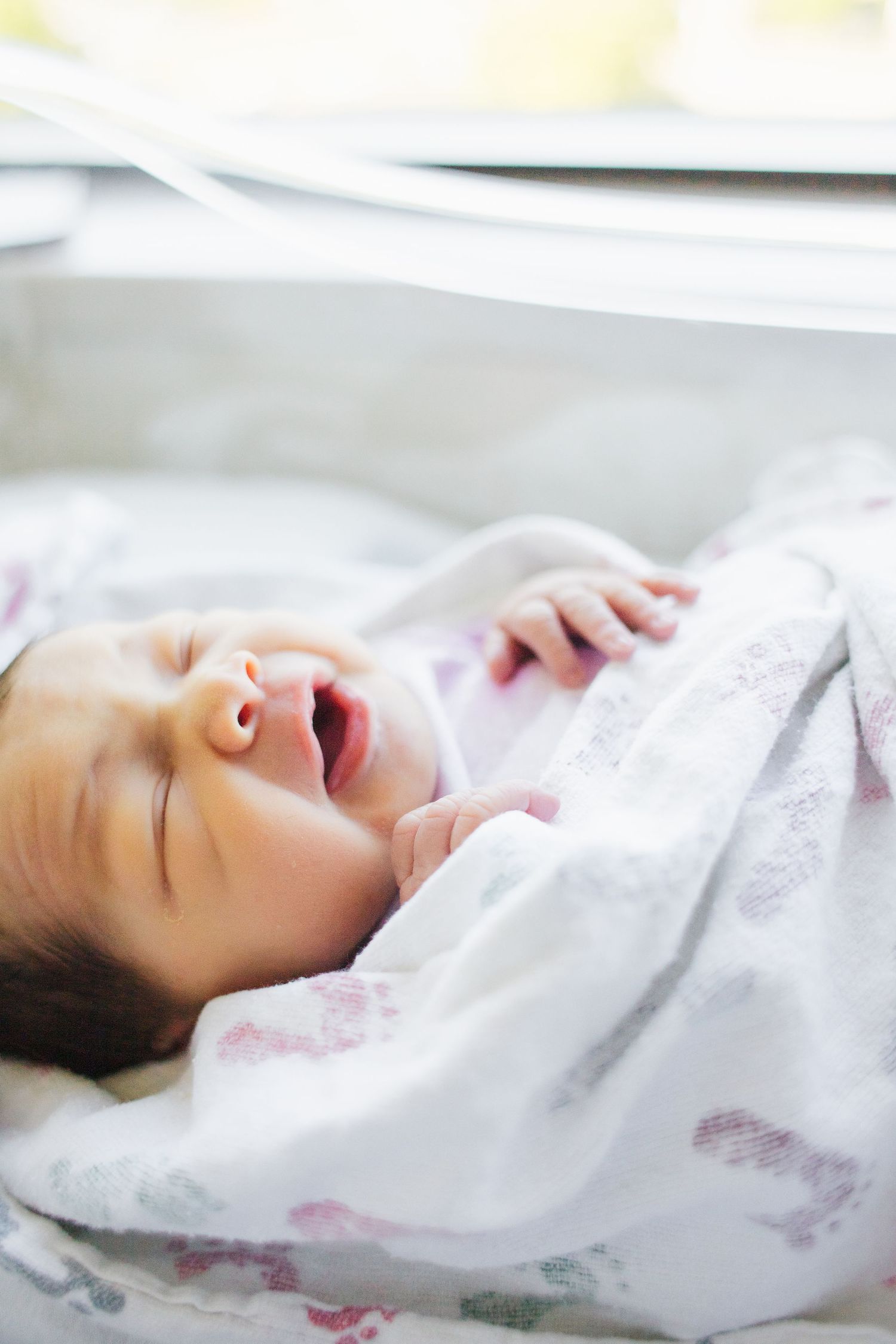 Newborn baby sleeping peacefully on white bedding with soft lighting.