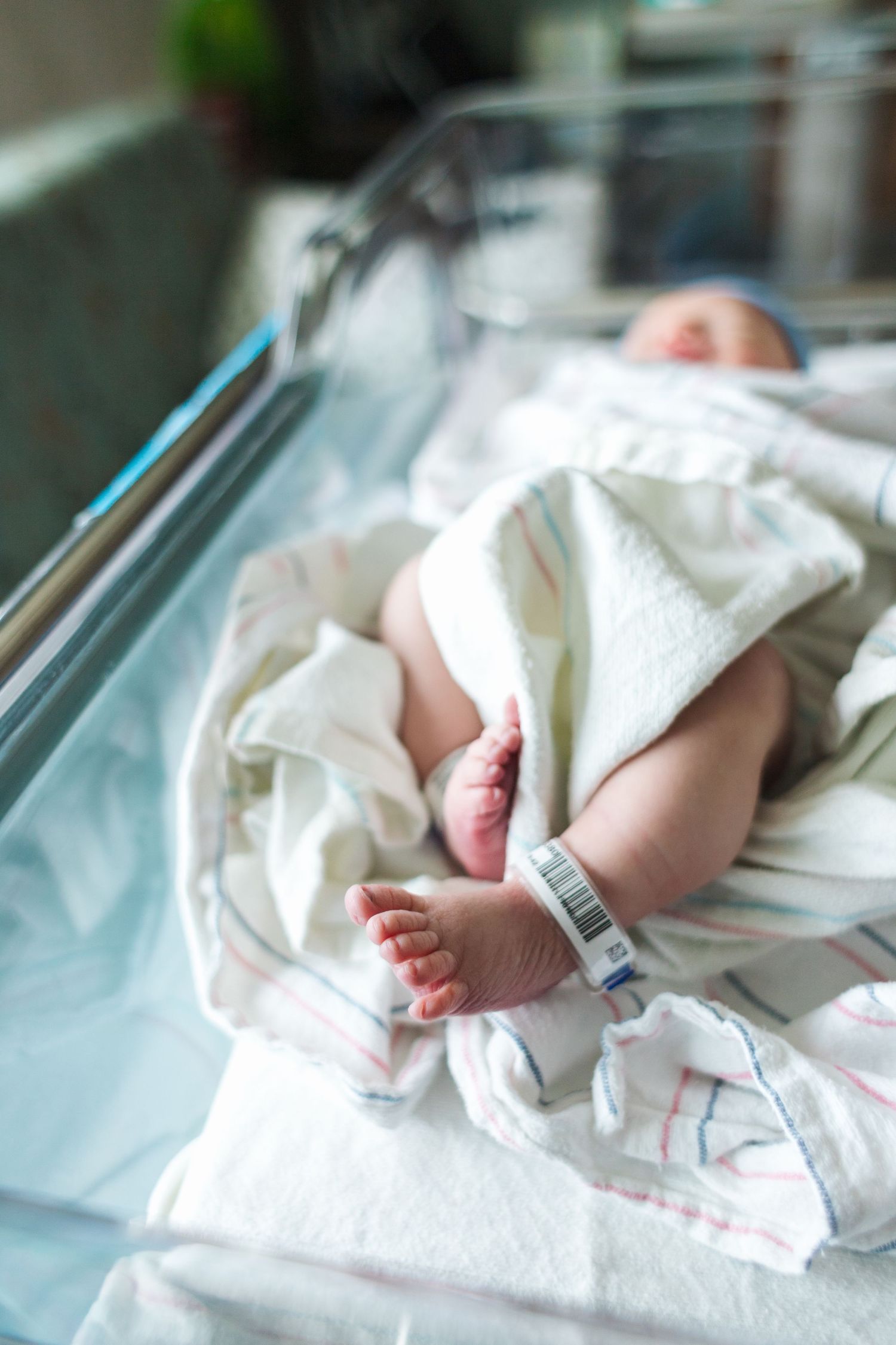 Tiny feet with hospital ID bands visible in clear hospital bassinet.