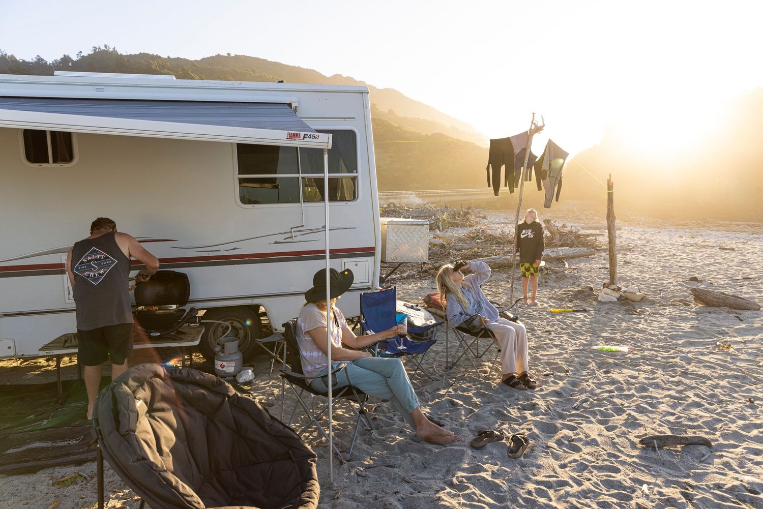 Friends gathering at beach campsite during sunset with RV in background.