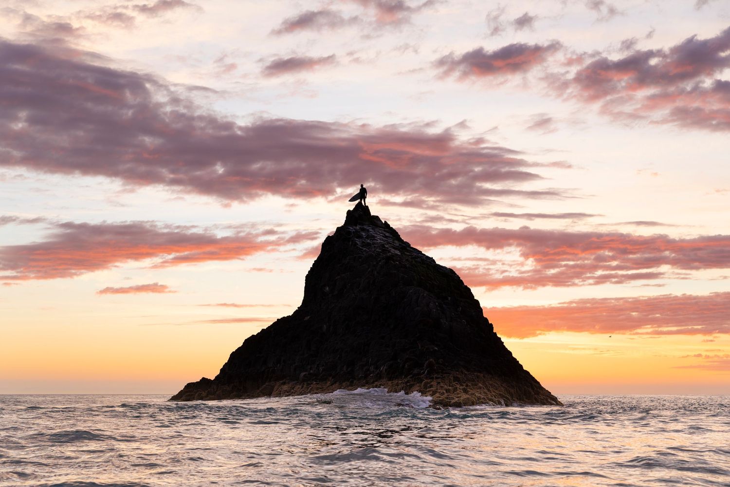 Panoramic sunset view of islands and rock formations in ocean with pink sky.