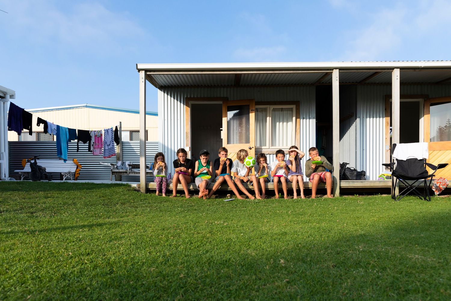 Row of beachside cabins with people relaxing on a grassy lawn.