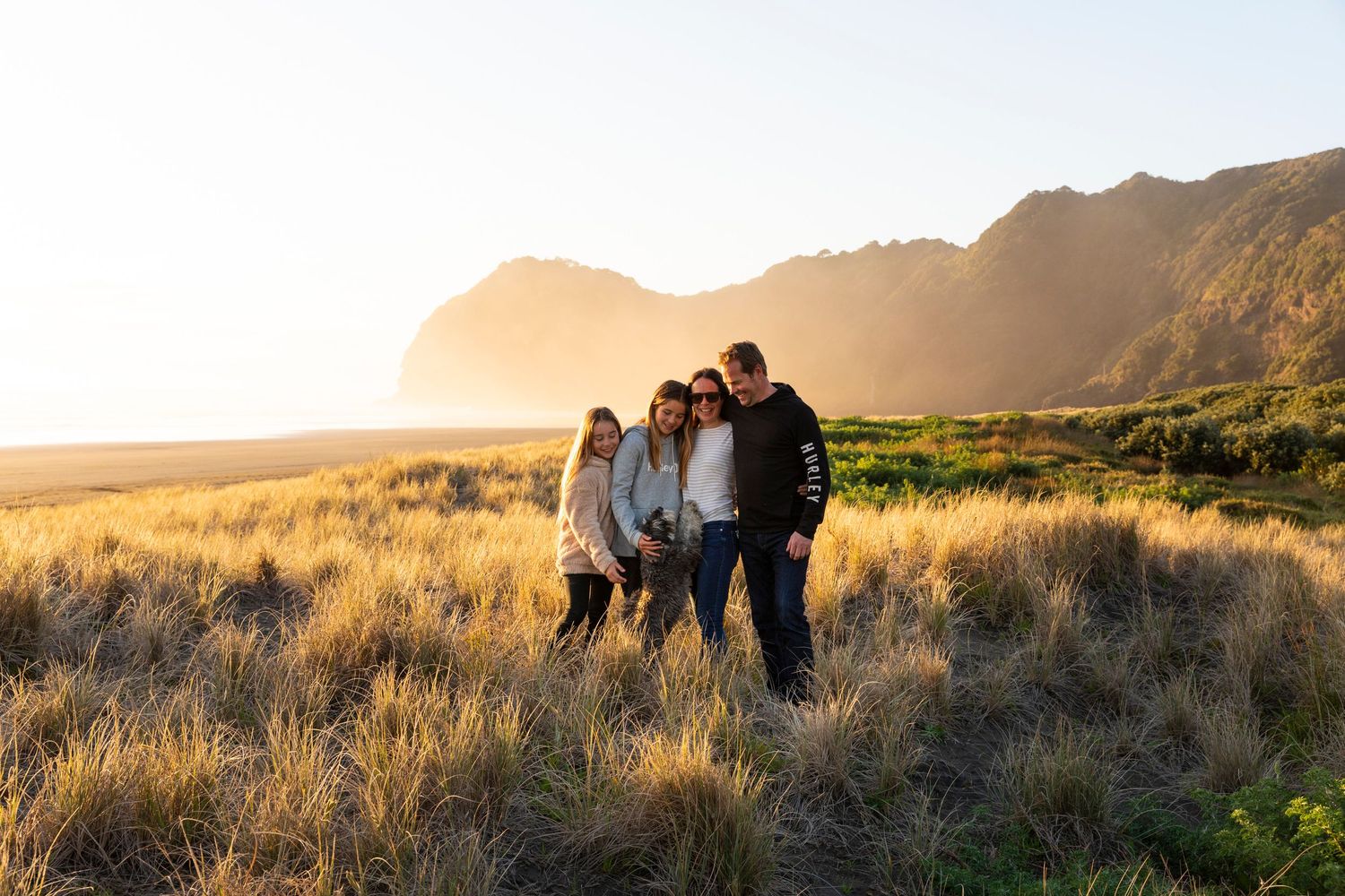Golden hour landscape photograph of people silhouetted against mountain backdrop at sunset.